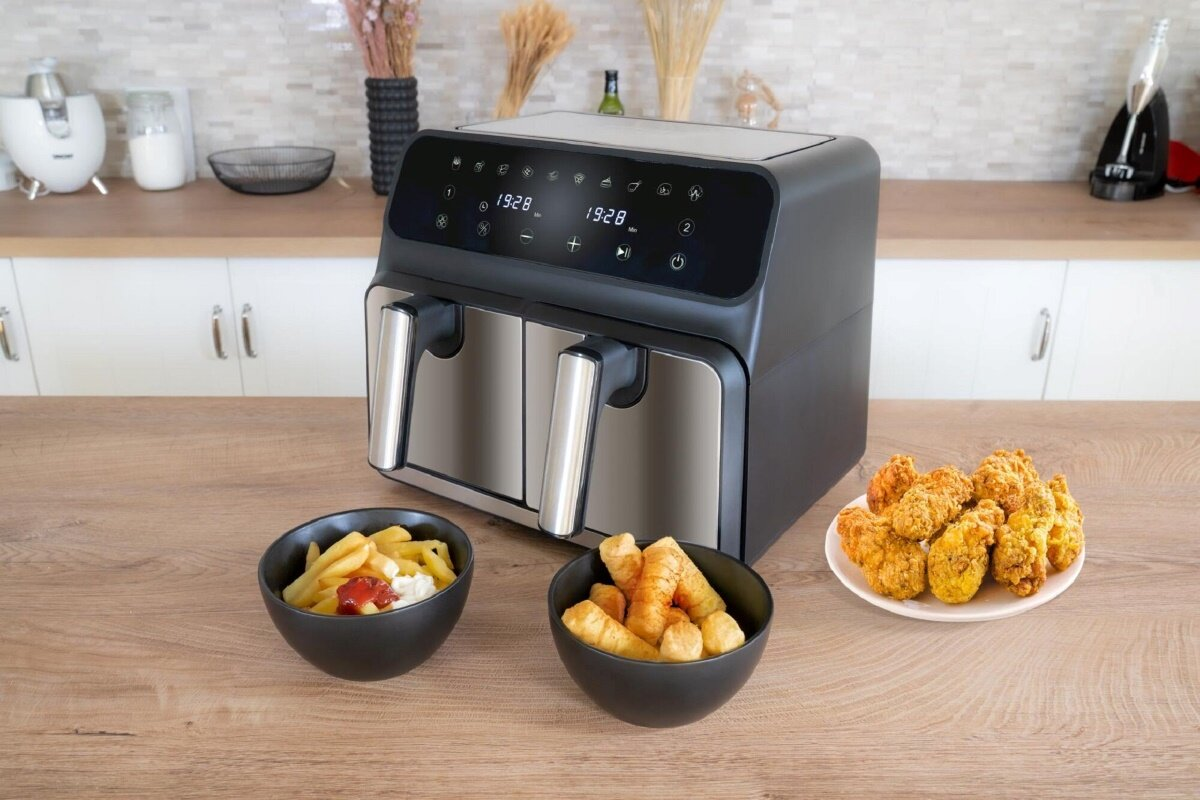 Czarna i srebrna frytkownica powietrzna z smażonym jedzeniem na stole, z dwiema miskami.