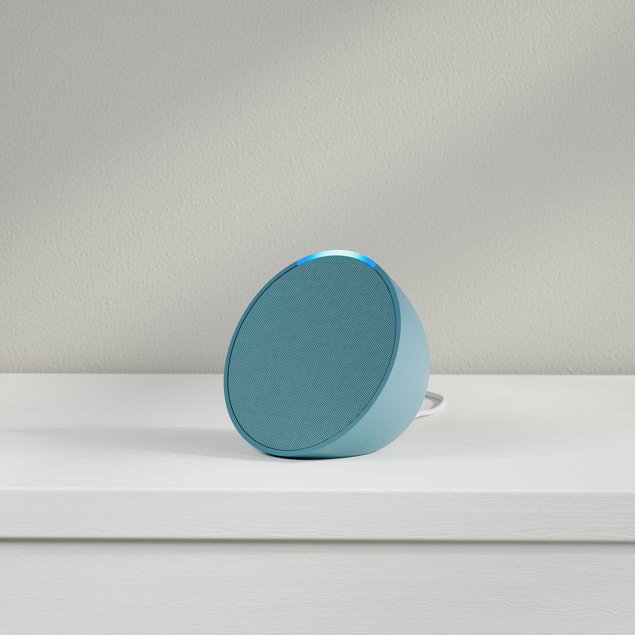 Ein blauer Smart-Lautsprecher auf einer weißen Oberfläche, mit hellblauem Leuchten oben.