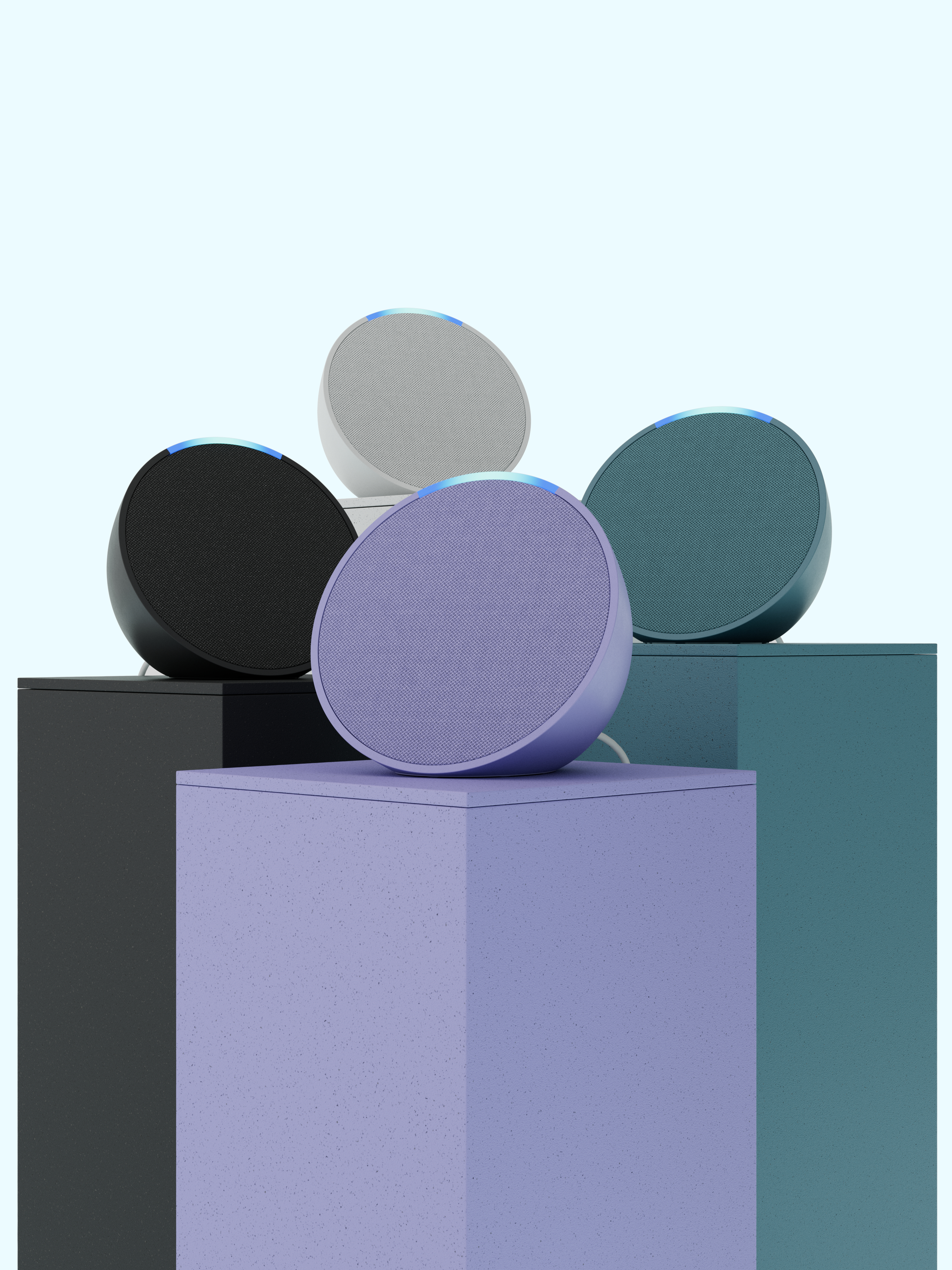 Fünf Smart Speaker in einer Reihe, in Schwarz, Weiß, Grau und Lila, auf Ständern mit hellblauem Hintergrund.