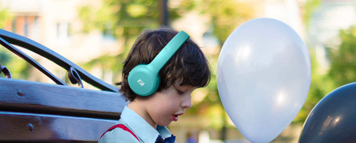 Ein kleiner Junge mit blauen Kopfhörern, der nach unten schaut. Zwei Luftballons im Hintergrund.