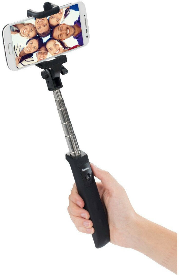 Dłoń trzyma wysuwany kijek do selfie z telefonem pokazującym grupę ludzi.