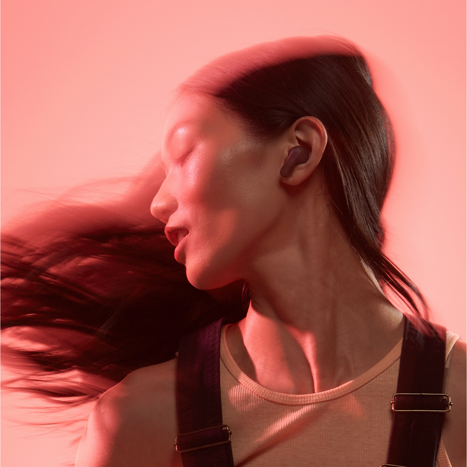 A woman with dark hair wearing purple earbuds, with a red background.