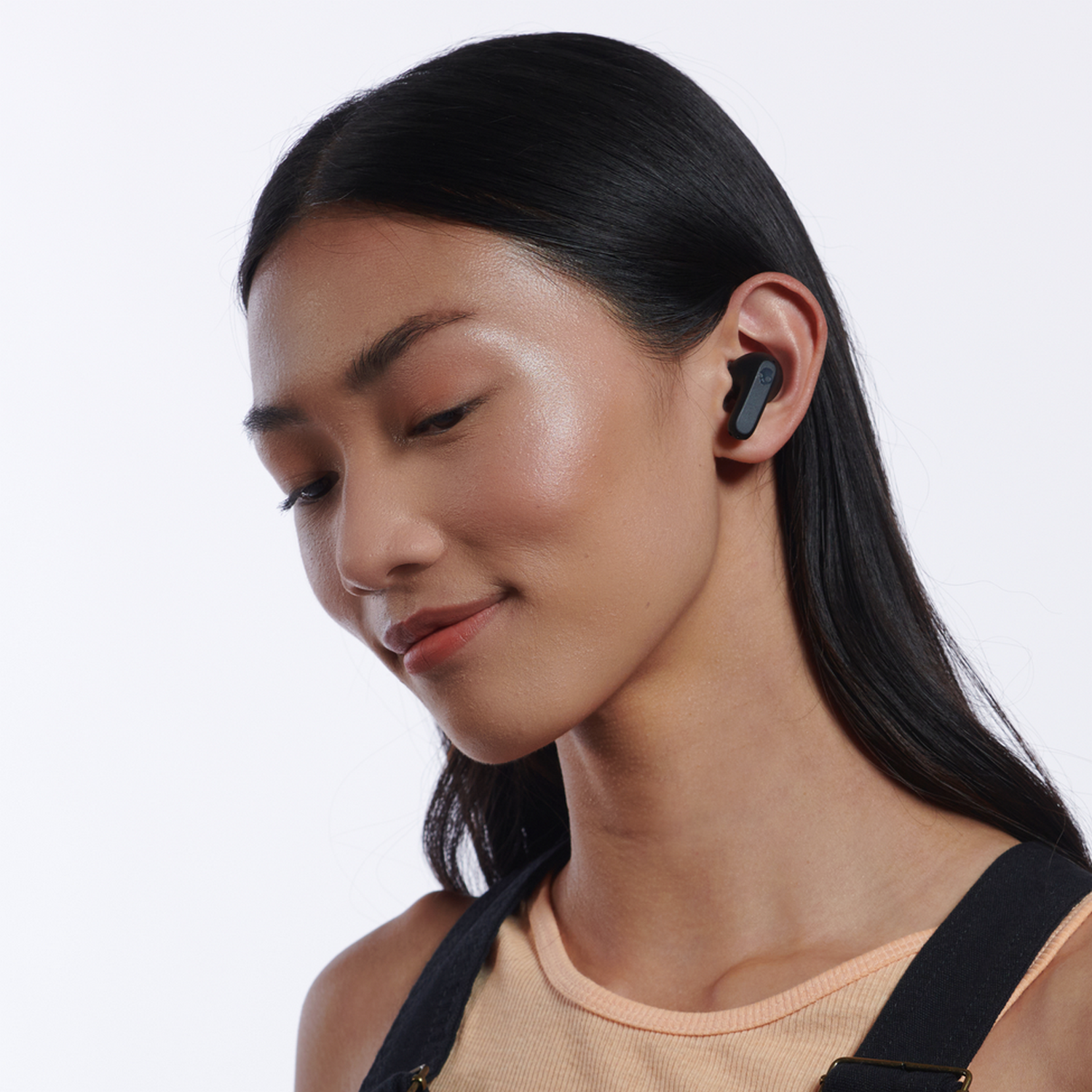 A woman with an earbud in her ear. She's wearing a beige top and looking down.