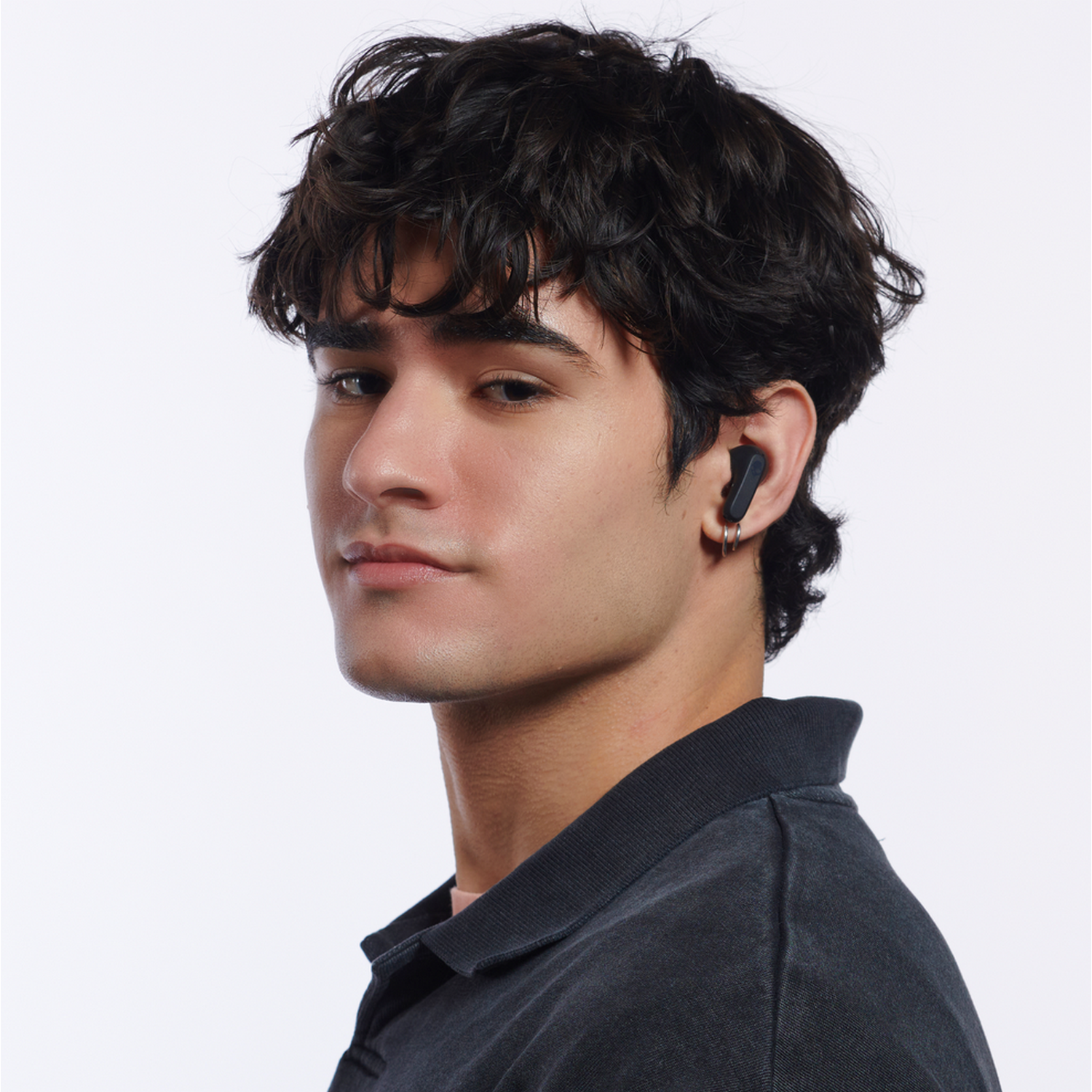 A young man with black earbuds in his ear. He is looking at the camera.