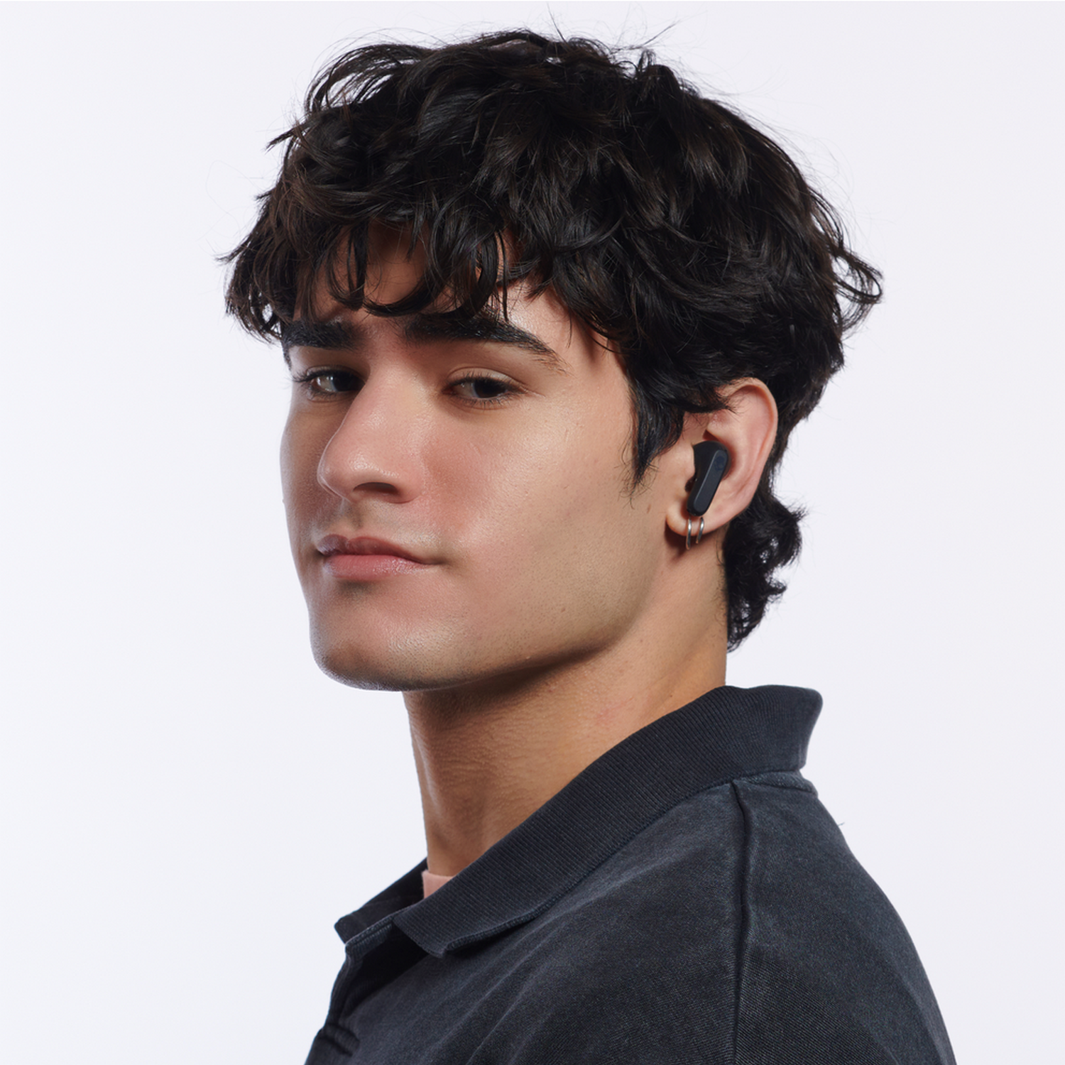 A young man with earbuds in, looking at the camera. White background.