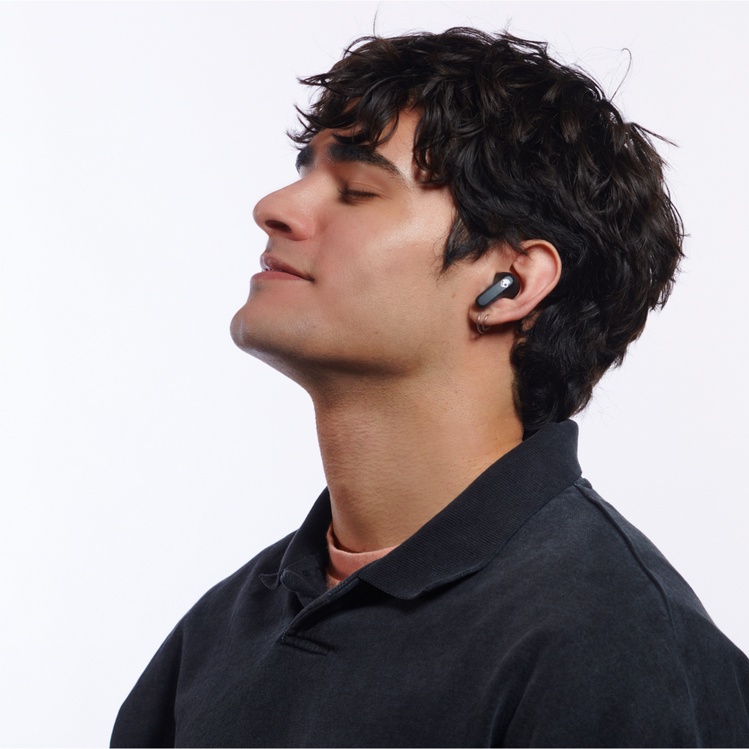 A man with dark hair wearing earbuds looks up with closed eyes, isolated against a white background.