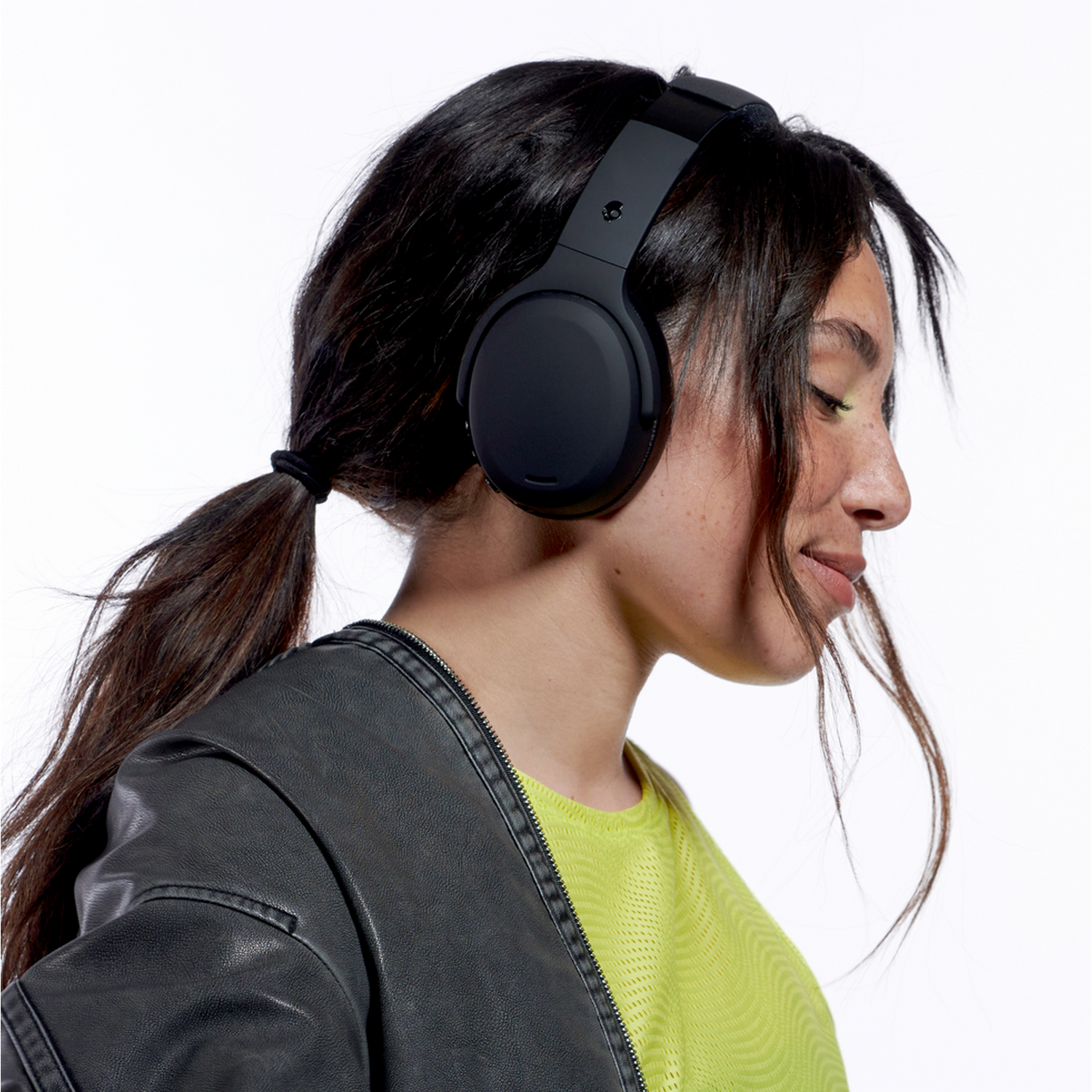 Woman wearing black Skullcandy headphones. She is wearing a yellow shirt and jacket.