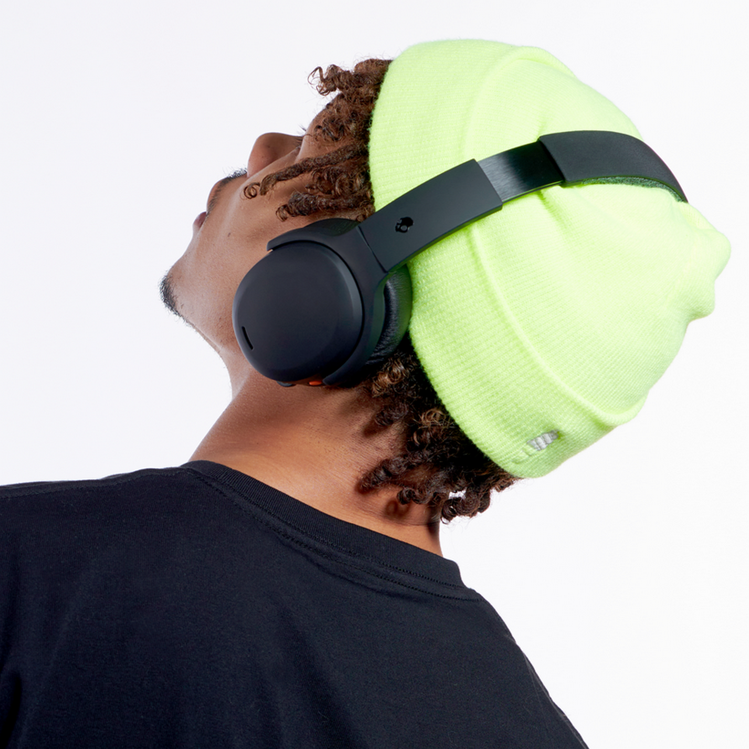 A man wearing a neon green beanie with headphones on, looking up.