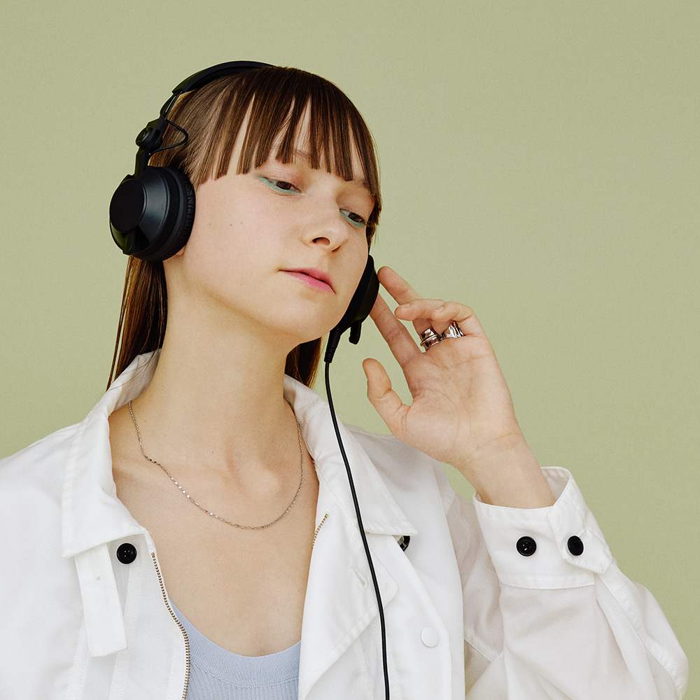 Femme portant un casque, une veste blanche et un collier. Fond vert.
