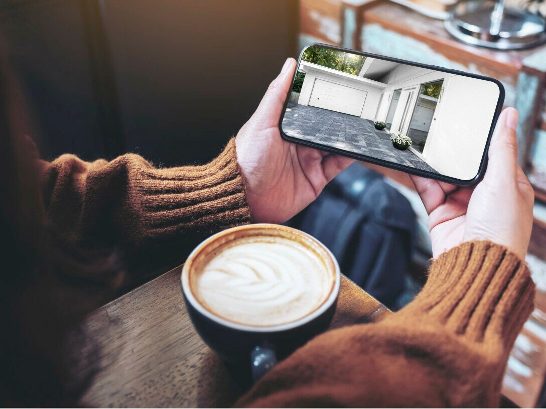 Osoba trzyma telefon pokazujący wnętrze domu z filiżanką kawy.