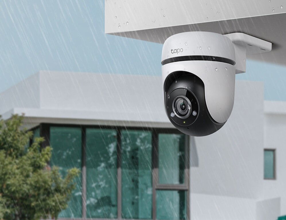 Biało-czarna kamera bezpieczeństwa na białym budynku, pada deszcz.