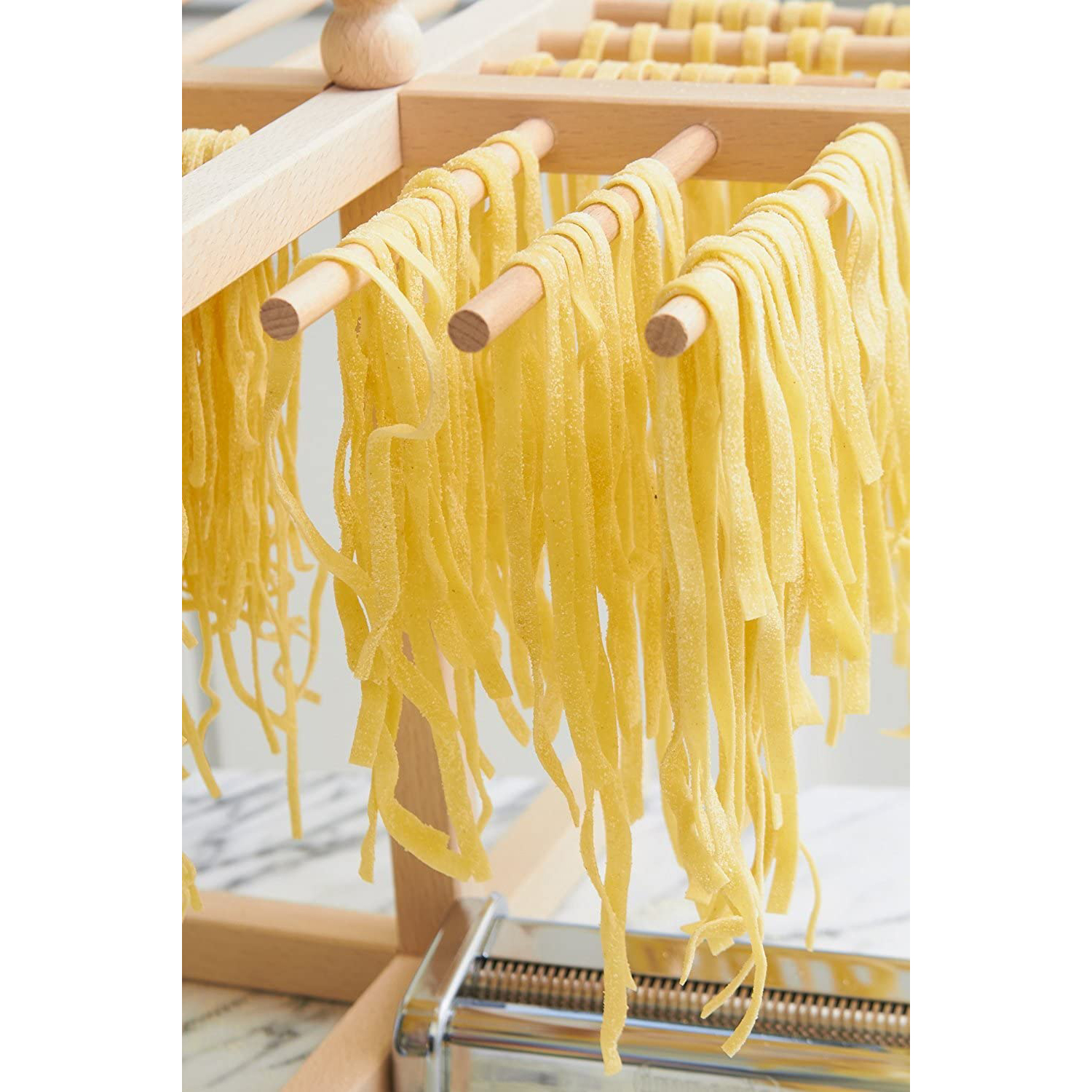 Pasta fresca appesa a un supporto di legno, pronta per l'essiccazione.