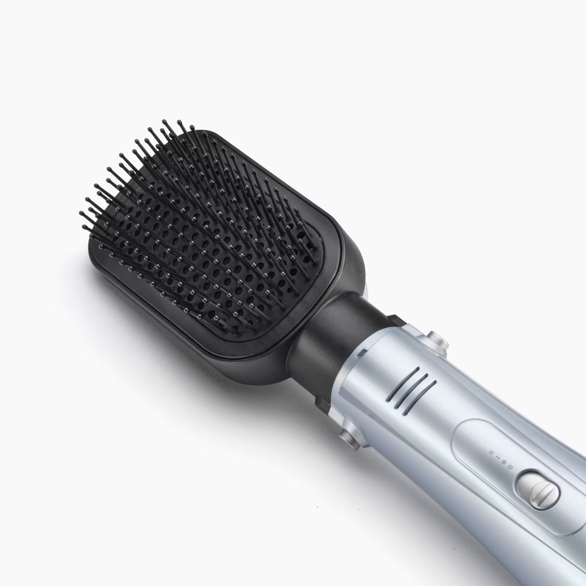 Cepillo para peinar el cabello con cerdas negras y mango plateado. Fondo blanco, vista en ángulo.