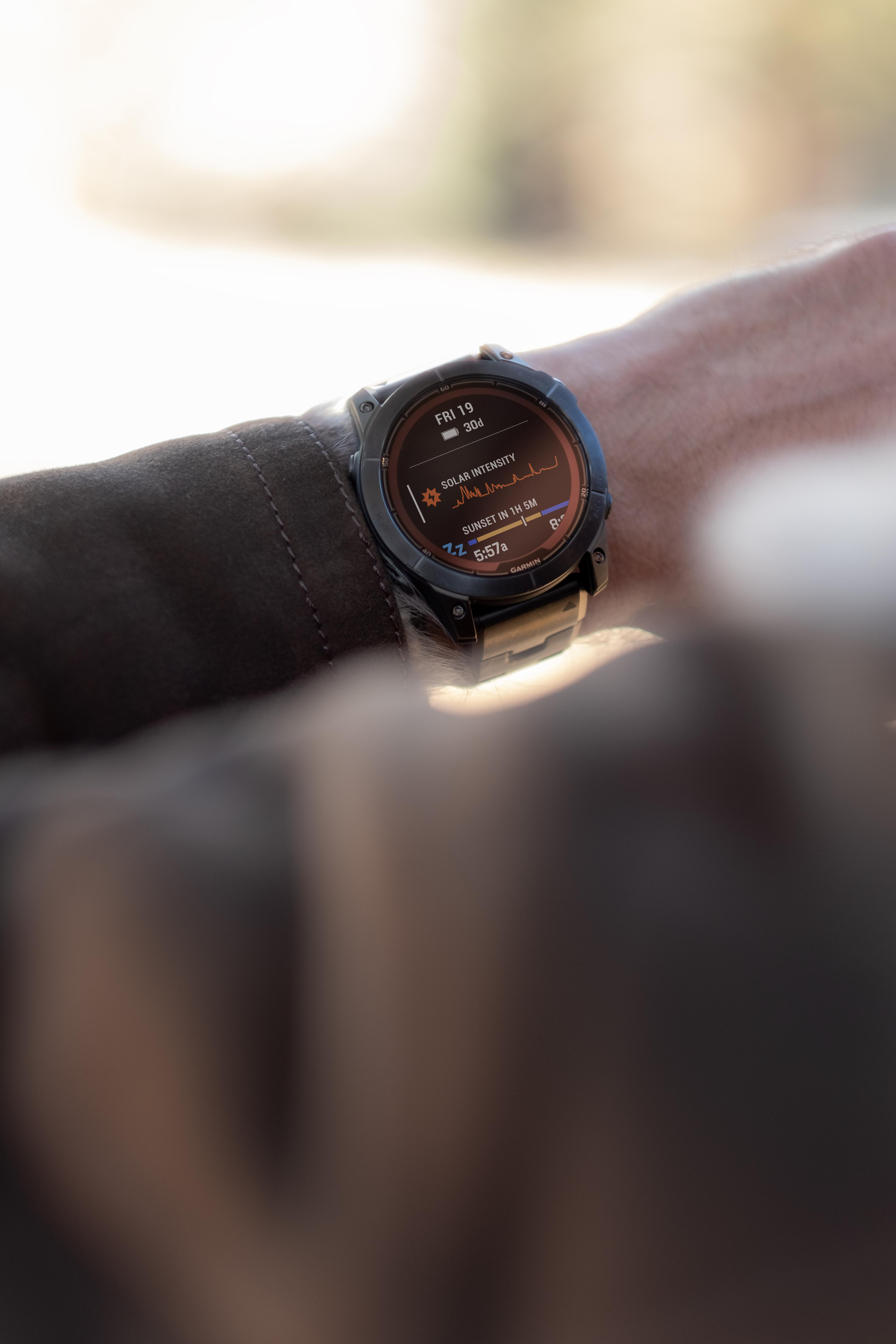 Ein Handgelenk zeigt eine Uhr mit Daten an. Der Hintergrund zeigt einen verschwommenen Arm und eine Landschaft.