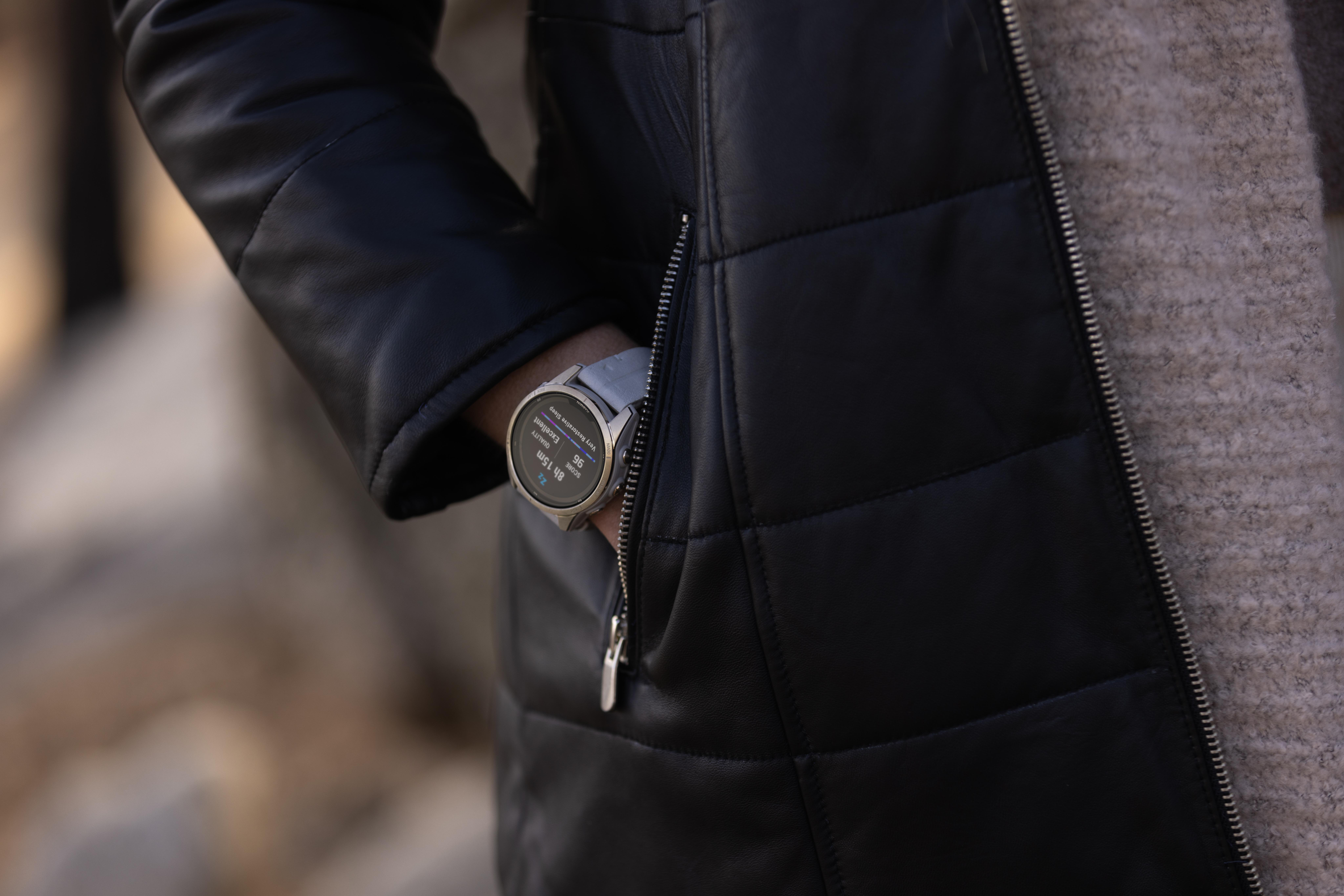 Person in schwarzer Jacke mit silberner Uhr, Hand in der Tasche. Hintergrund unscharf.