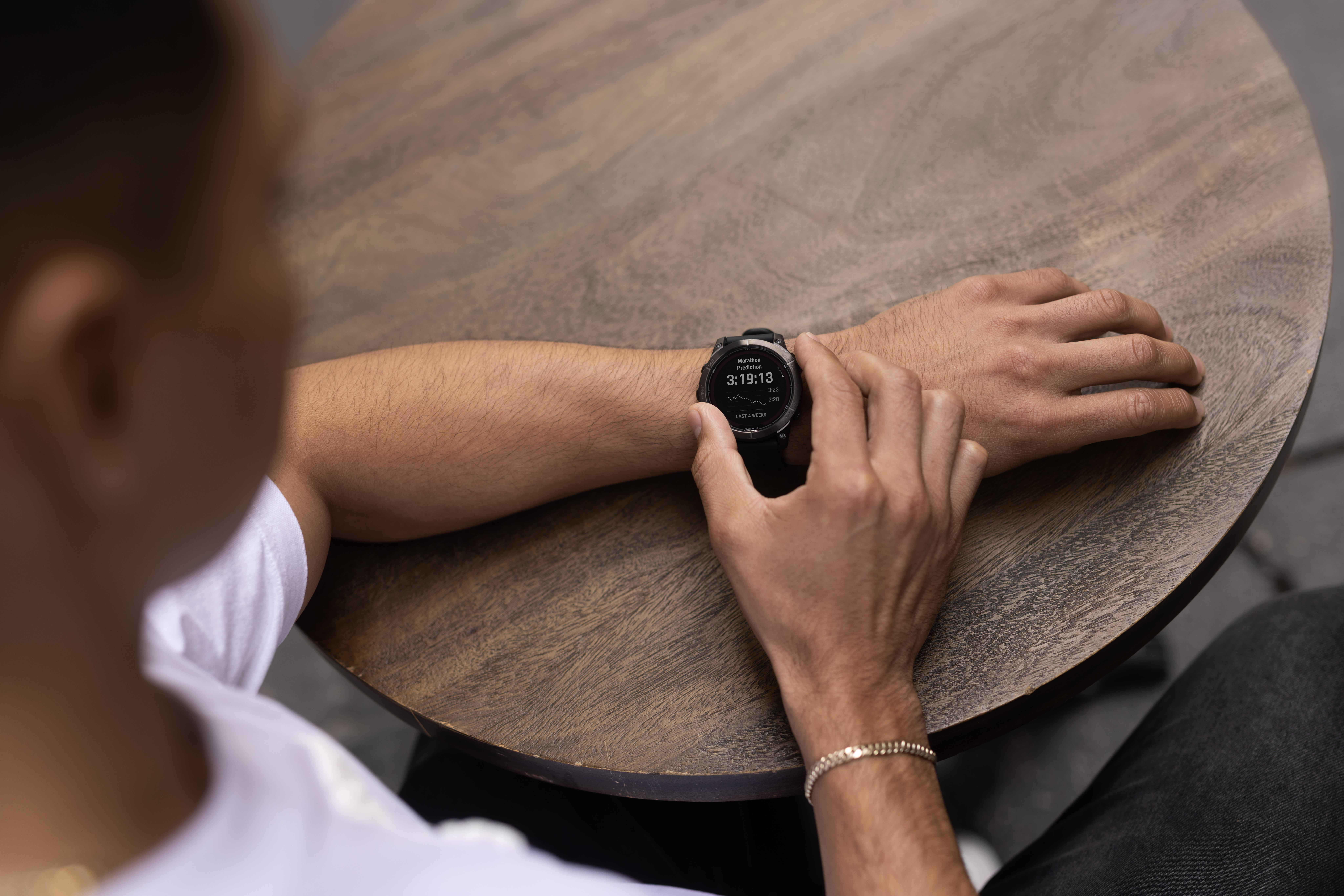 Person trägt eine Smartwatch auf einem runden Holztisch. Die Uhr zeigt Daten an.