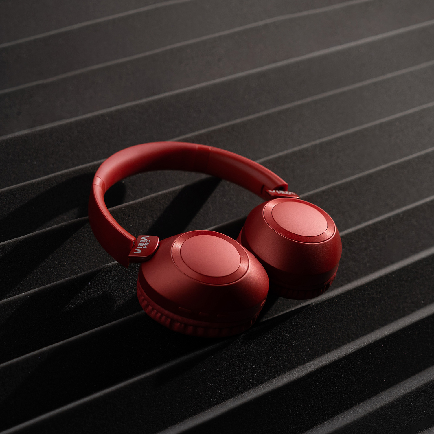 Auriculares rojos sobre la oreja sobre una superficie negra texturizada, creando un contraste visual.