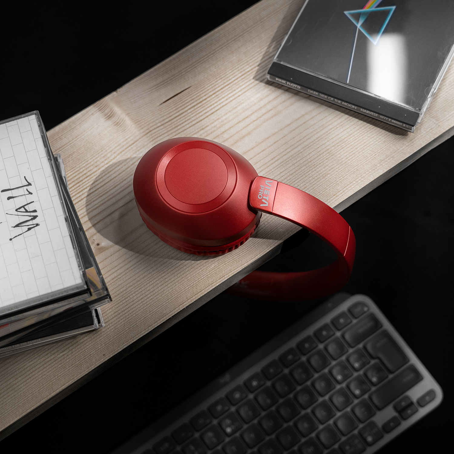 Auriculares rojos Viena Pro sobre una superficie de madera con álbumes de música y teclado de fondo.