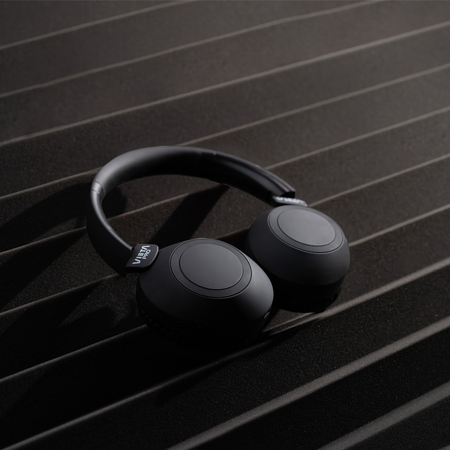 Auriculares negros sobre una superficie negra con crestas. Los auriculares son el foco.
