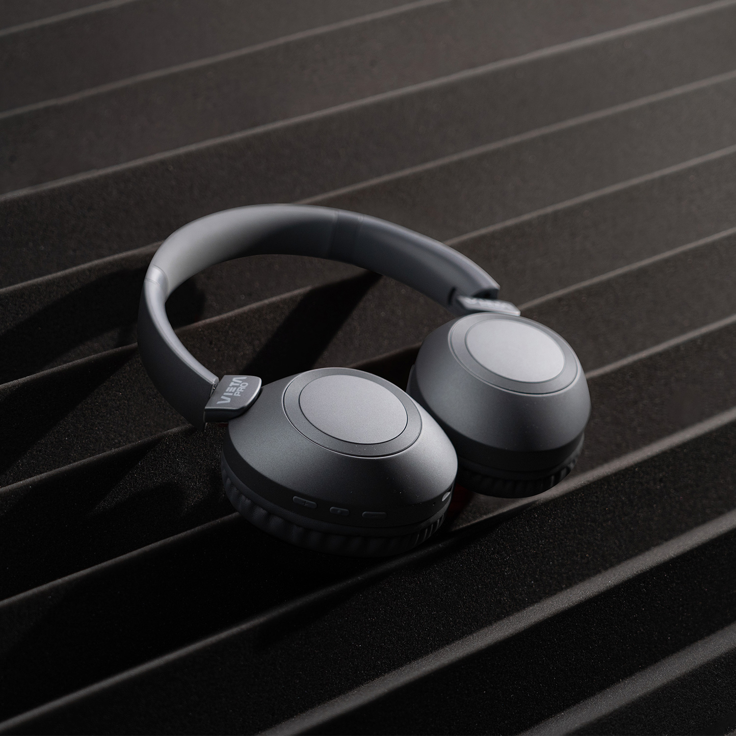 Auriculares grises apoyados en paneles de espuma insonorizante negros y texturizados.