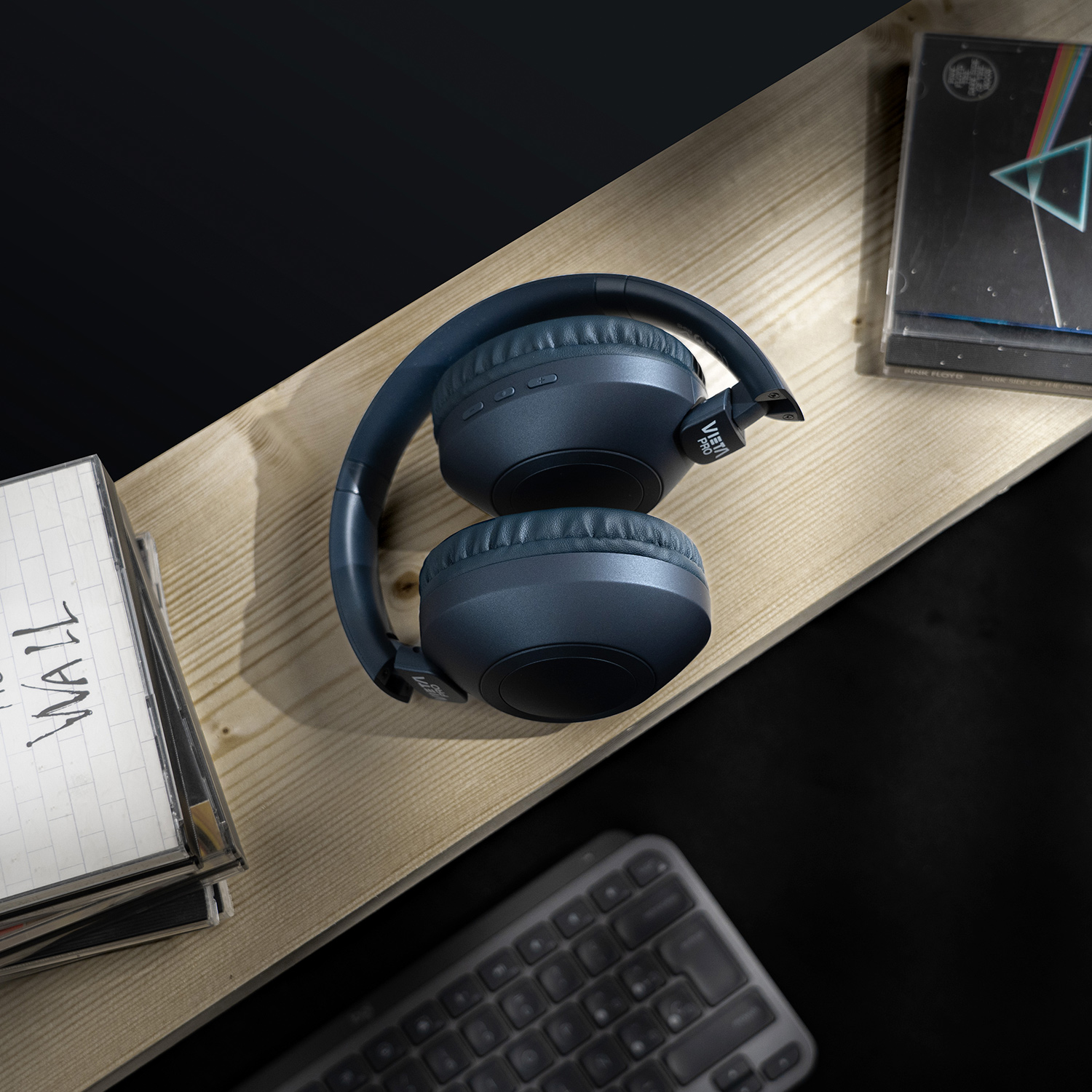 Auriculares azules plegados sobre una superficie de madera con cintas de cassette.
