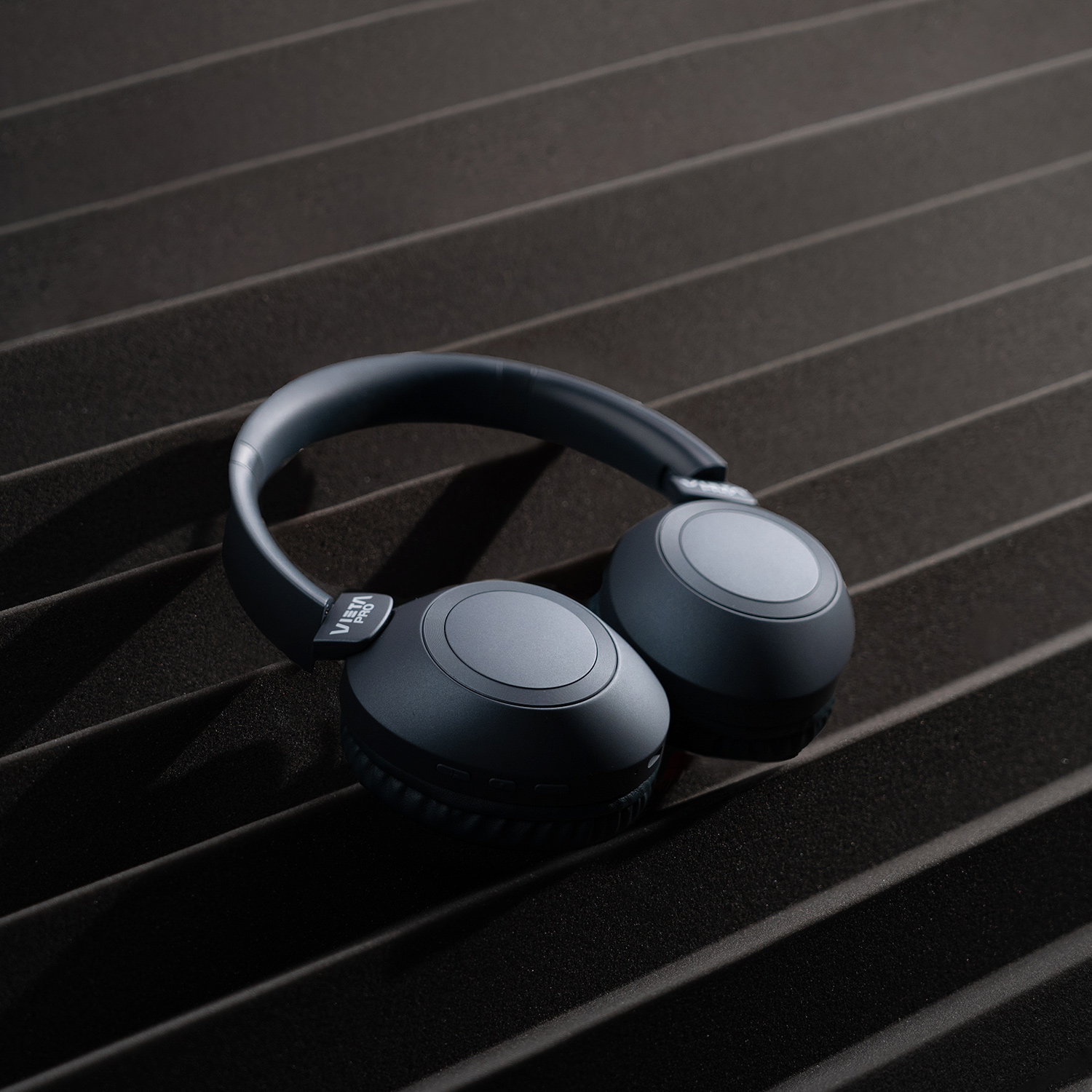 Auriculares gris oscuro sobre superficie texturizada, sobre fondo oscuro.