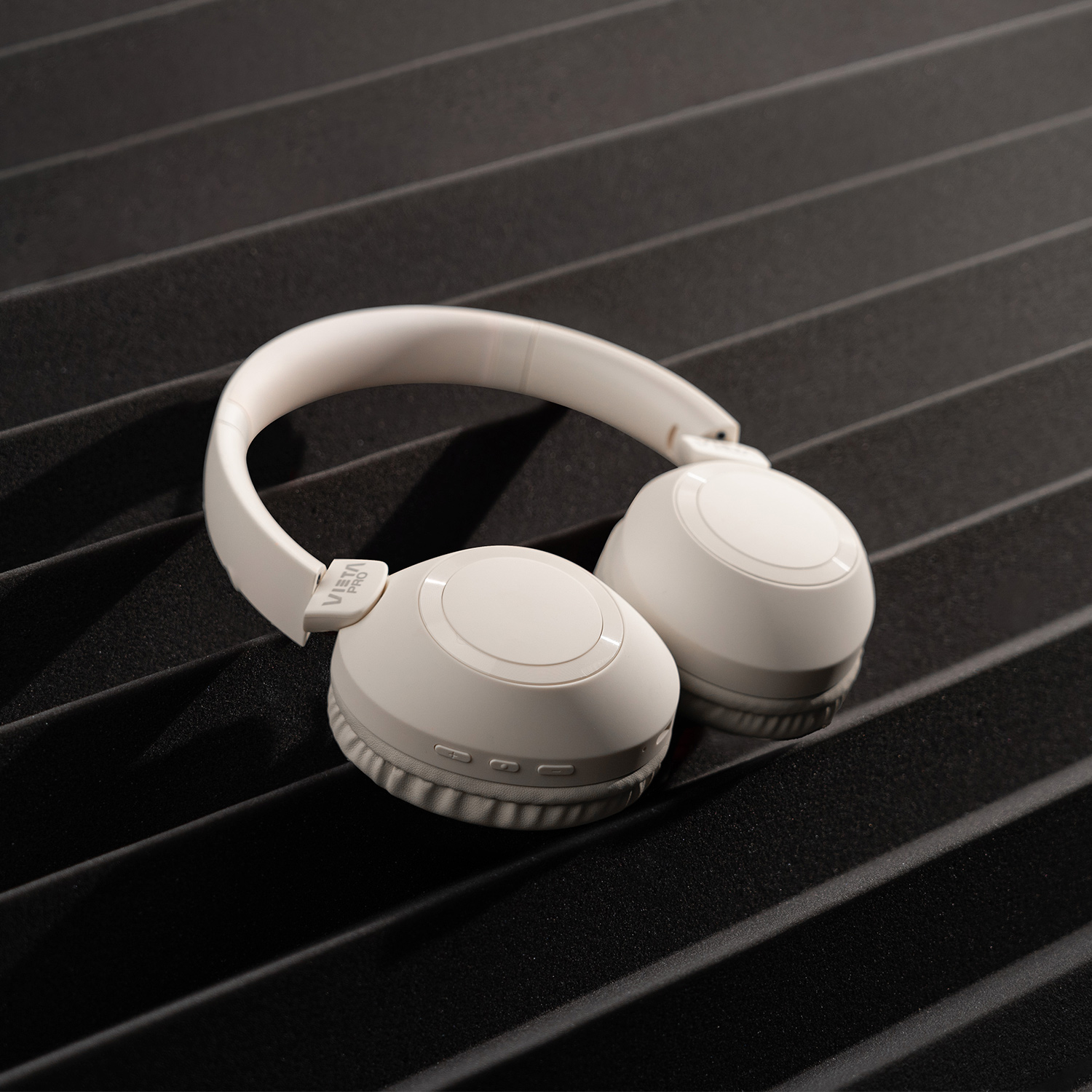 Auriculares blancos sobre un fondo negro texturizado. Los auriculares están centrados.