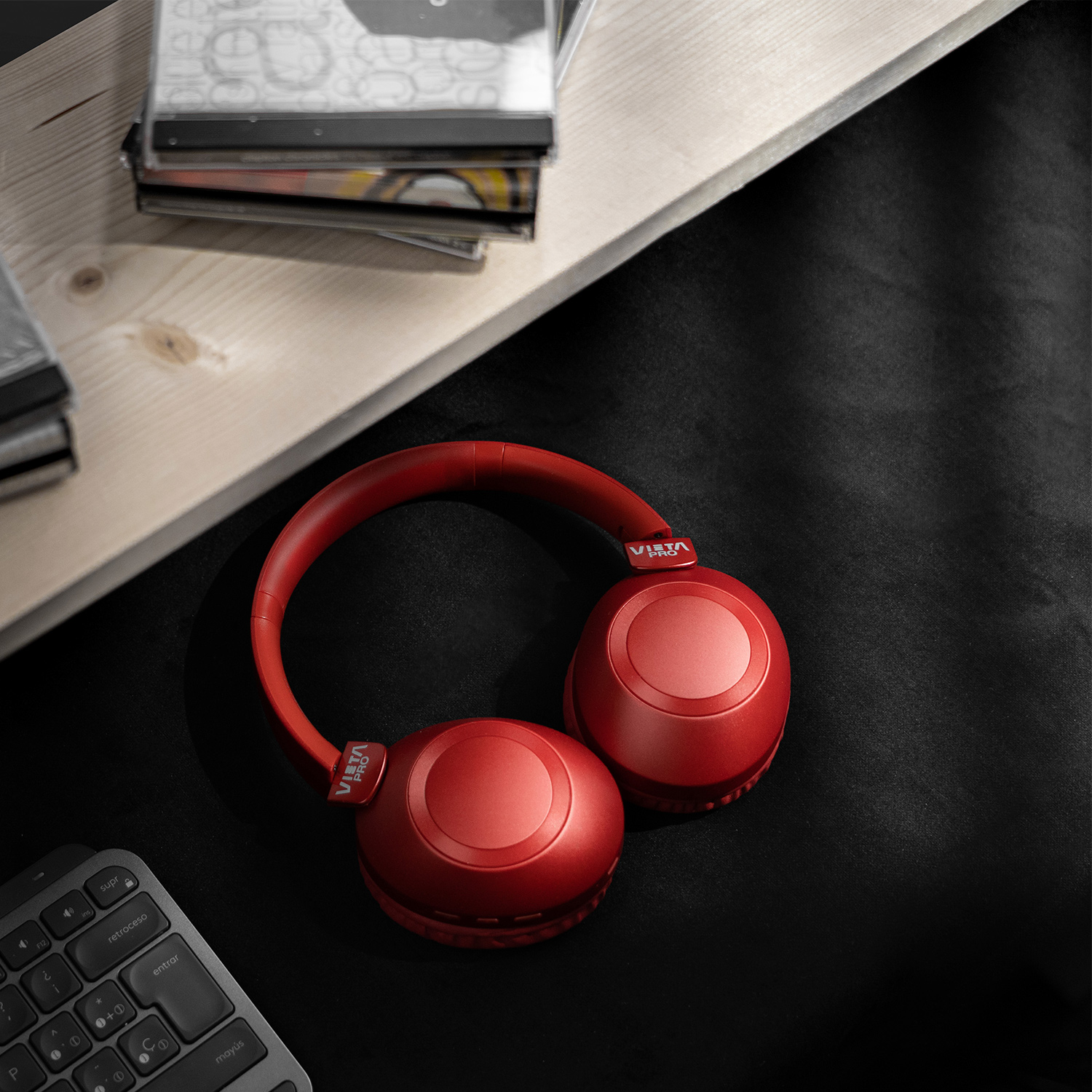 Auriculares rojos sobre una superficie negra, con un teclado y CDs al fondo.