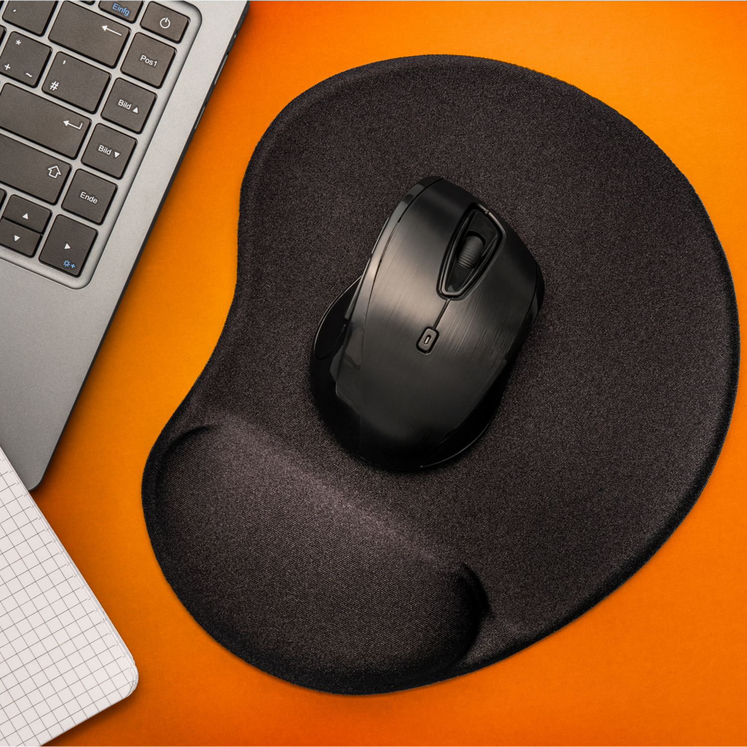 A black mouse on a black ergonomic mouse pad. A laptop is in the background.