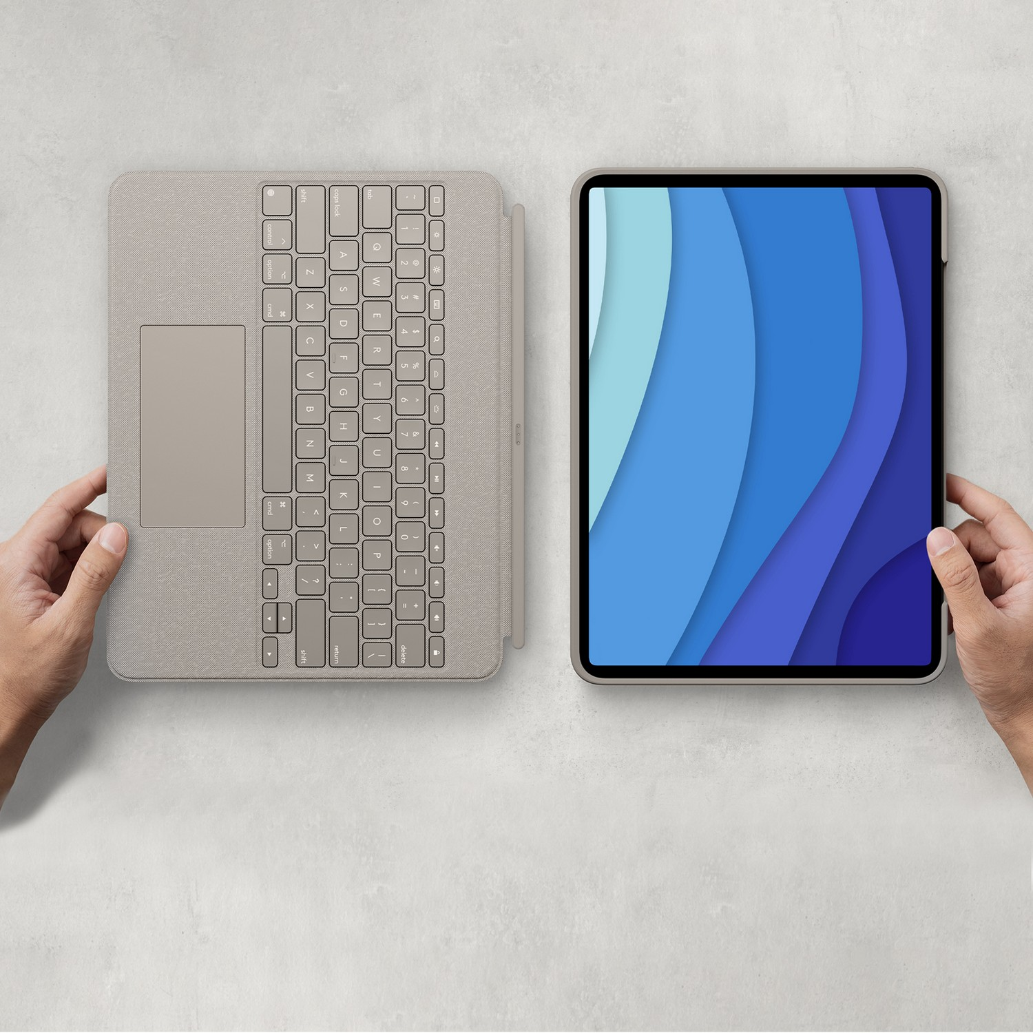 Mains tenant une tablette et un clavier. La tablette affiche un motif bleu en couches.