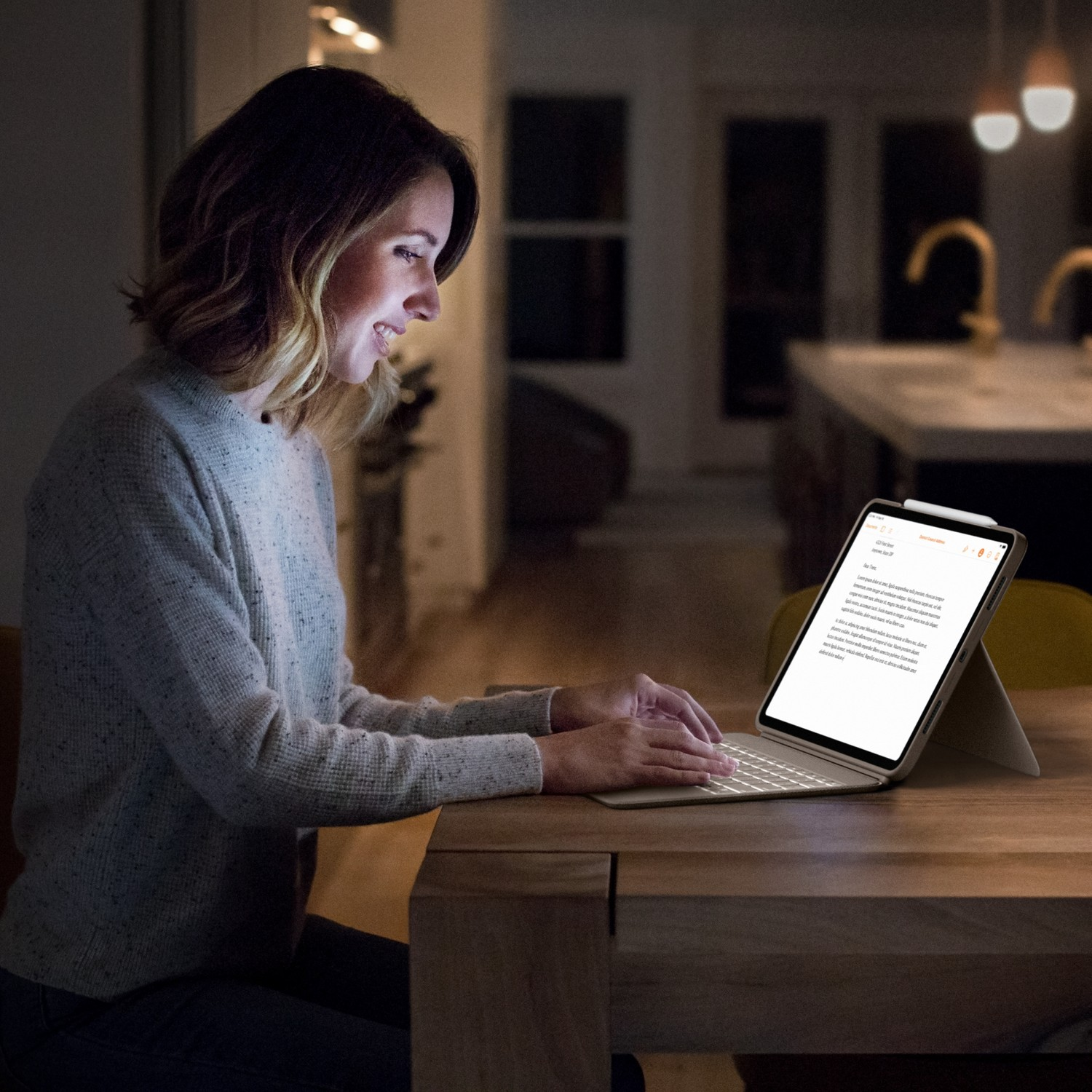 Femme à une table travaillant sur une tablette allumée dans une pièce sombre.