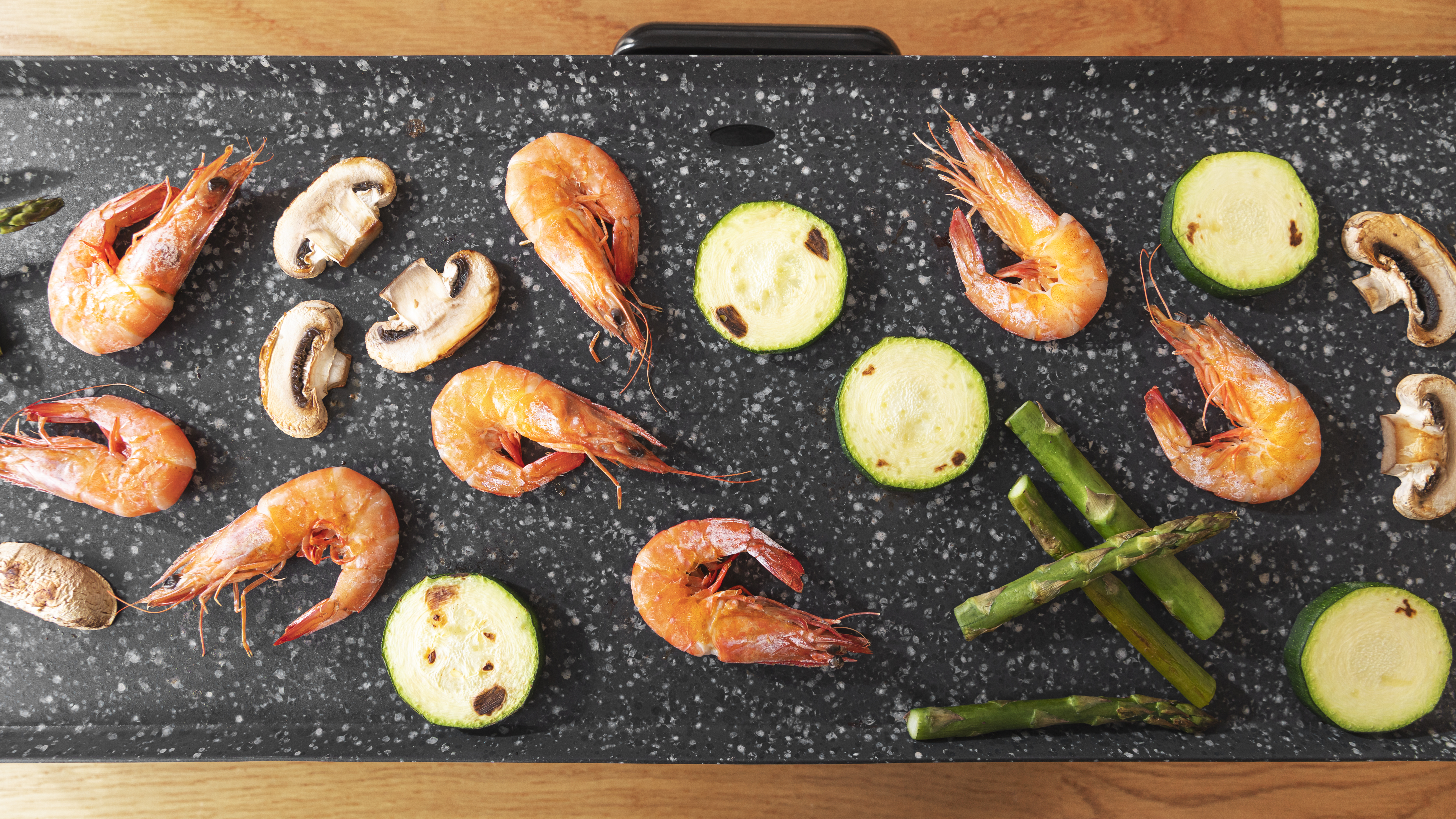 Gambas, verduras y champiñones a la plancha sobre una plancha negra.