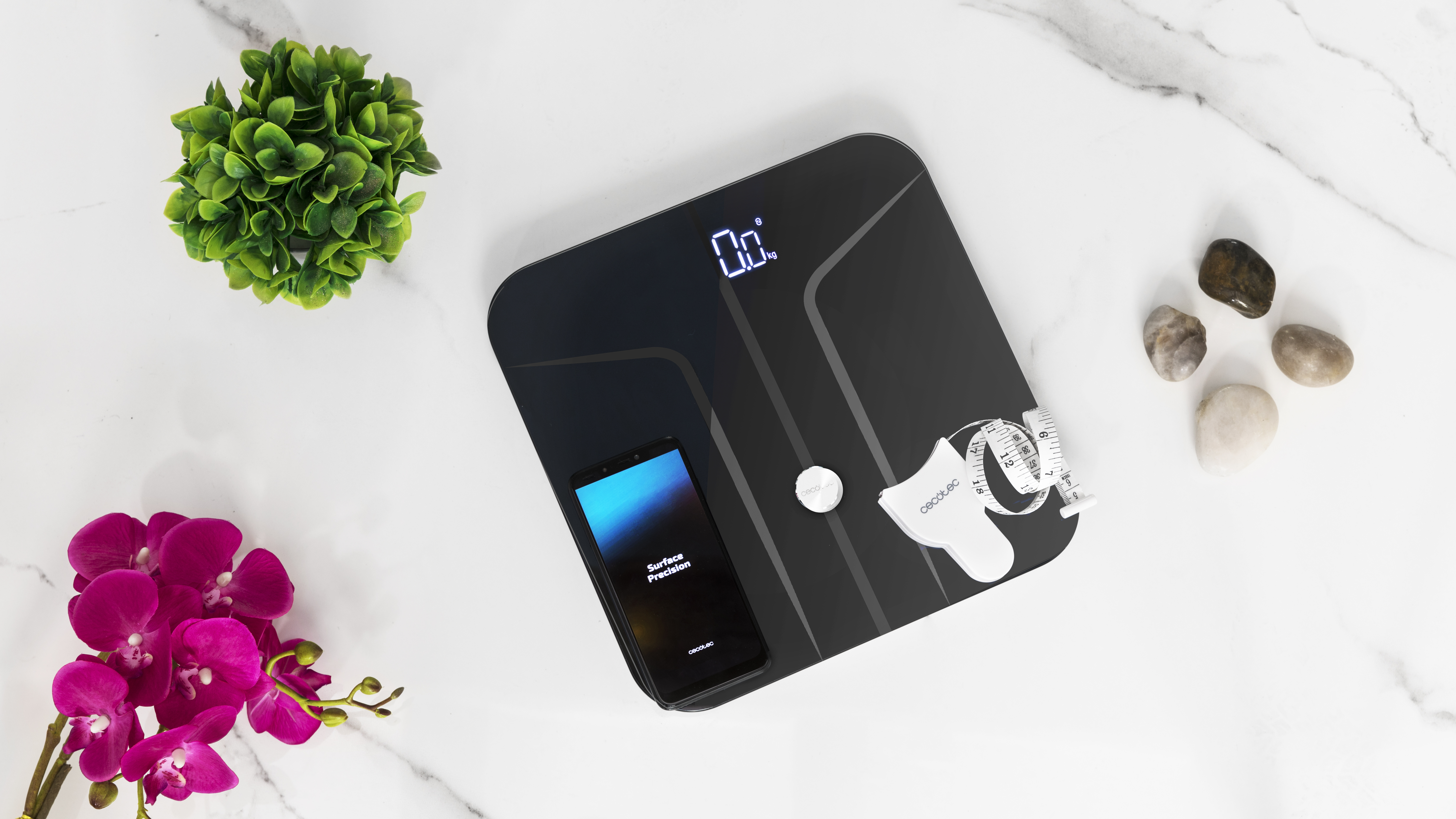 Una báscula negra con un teléfono, una toalla y elementos decorativos.