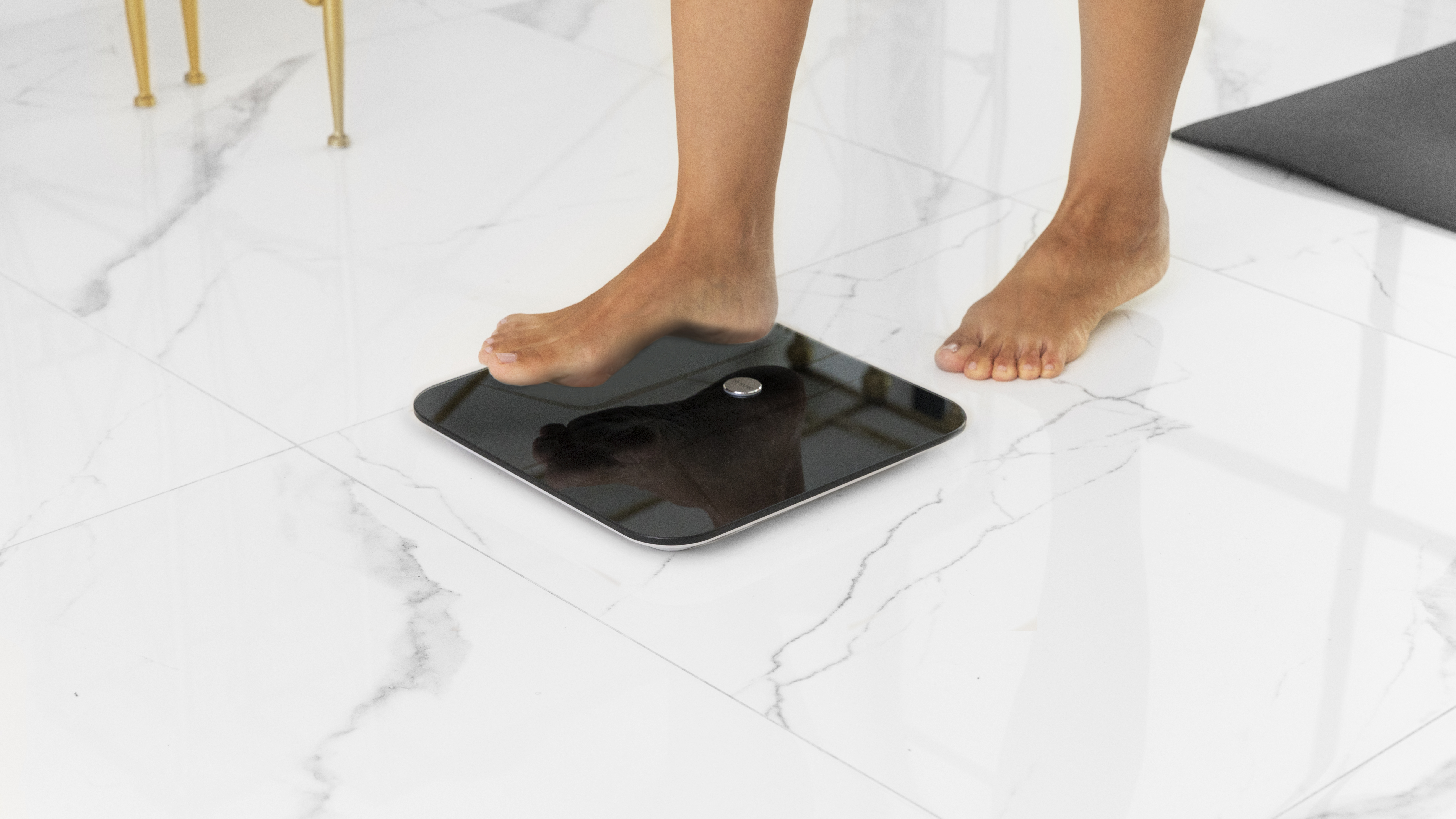 Pies sobre una báscula digital, reflejando el cuerpo, en un suelo de mármol blanco.