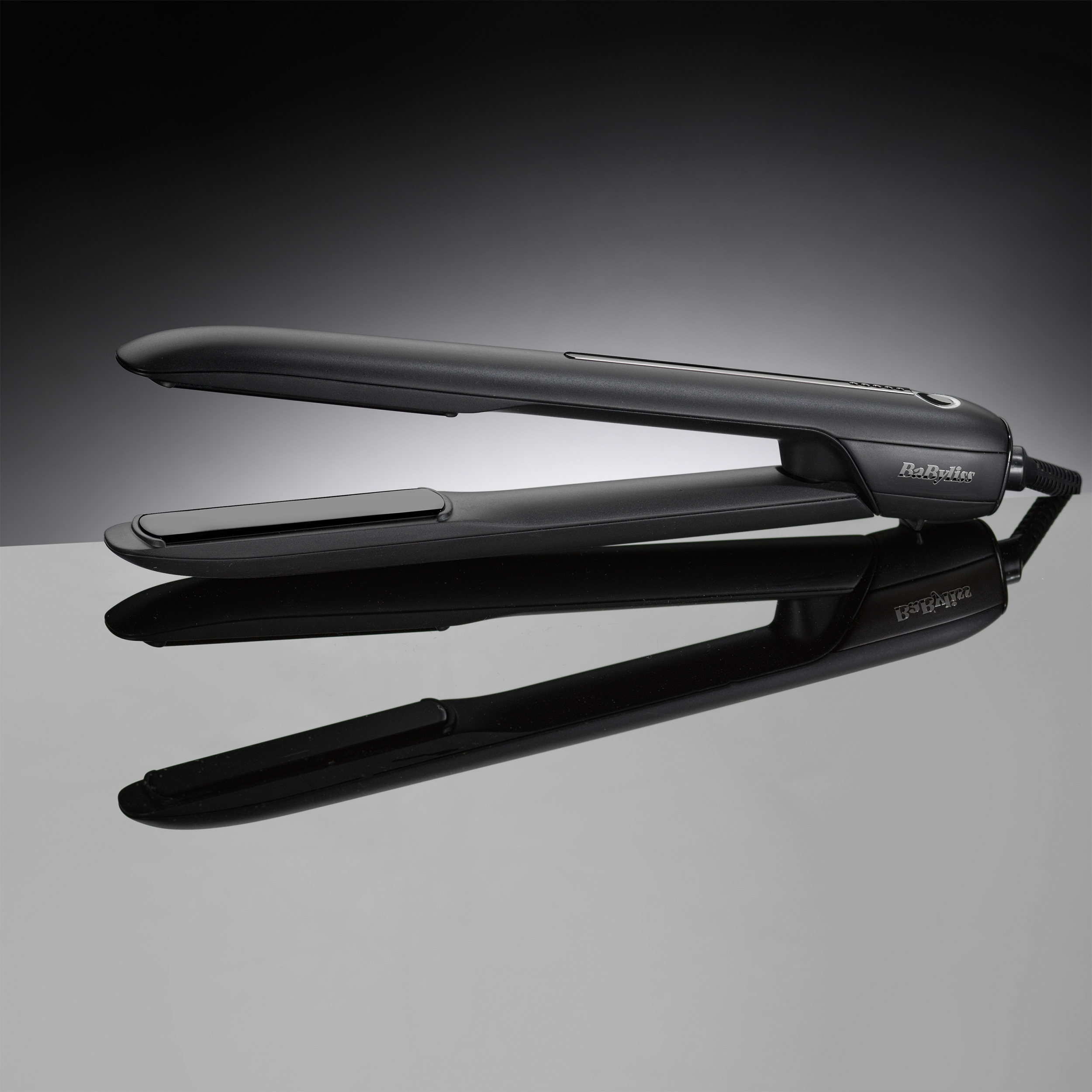 Plancha de pelo negra sobre una superficie reflectante. Es un producto de belleza.