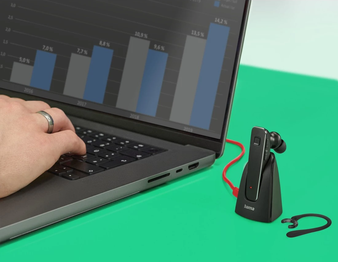 Main utilisant un ordinateur portable avec un graphique à l'écran. Un casque connecté avec une station de charge est visible.