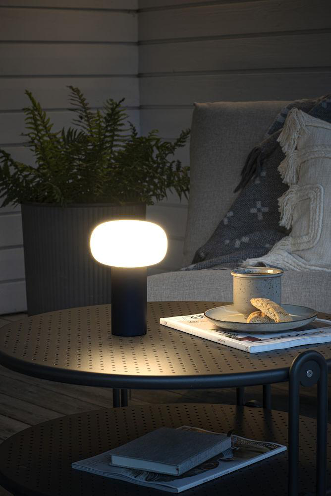Szene im Freien mit einer Lampe auf einem Tisch. Eine Pflanze und eine Kaffeetasse sind ebenfalls vorhanden.