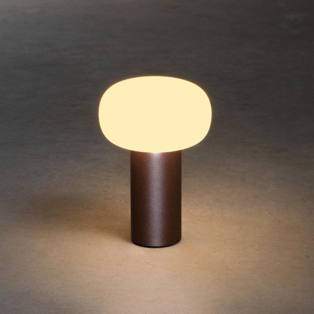 Eine braune Lampe mit einem weißen, ovalen Licht oben steht auf einer braunen Oberfläche und wirft einen sanften Schein.