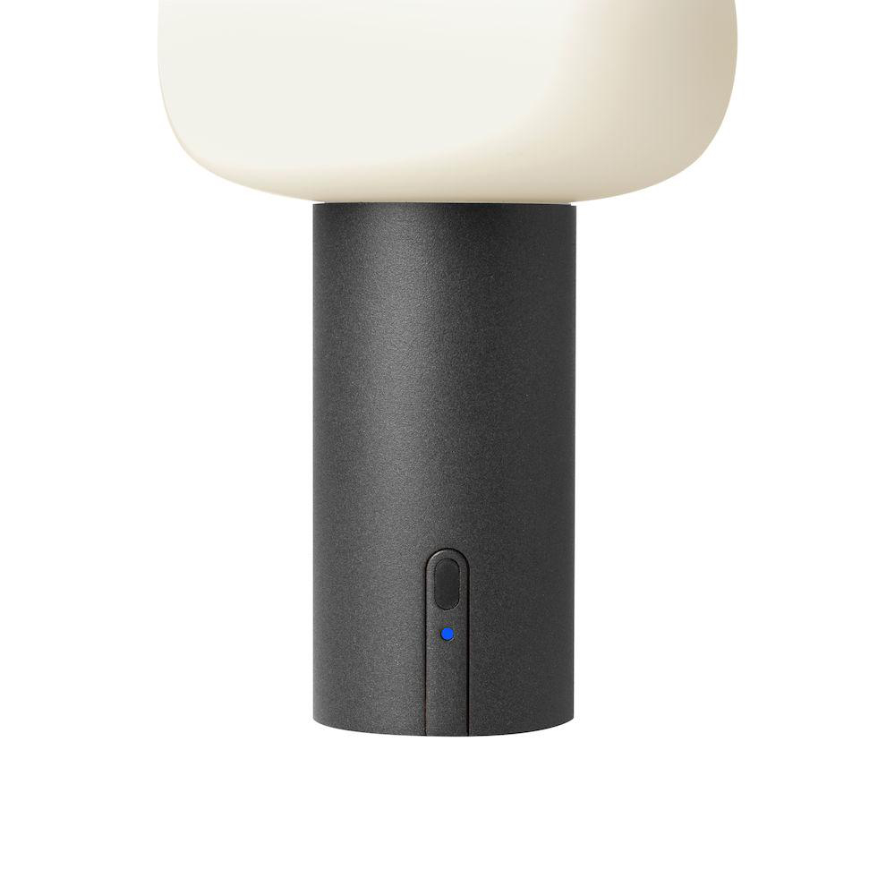 Eine schwarze zylindrische Lampe mit weißem Oberteil und blauem Einschaltknopf.