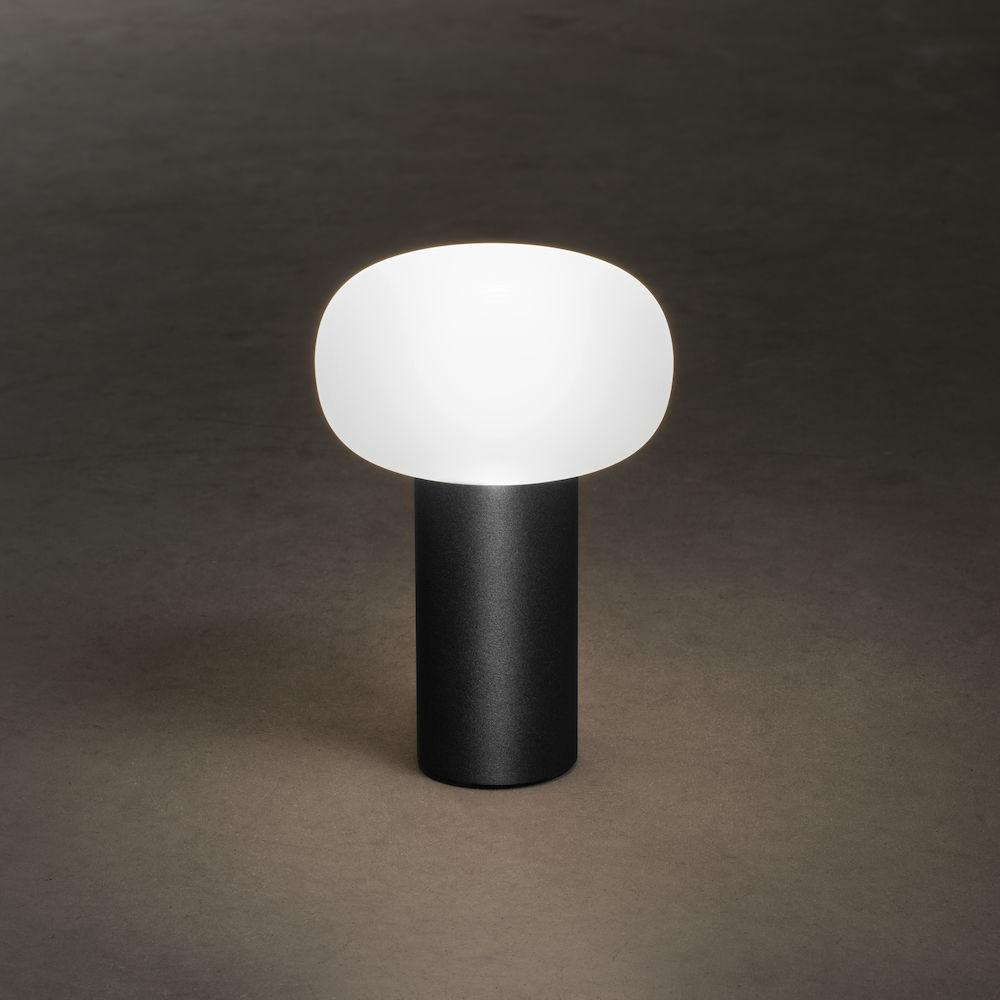 Schwarz-weiße Tischlampe mit ovalem, weißem Lampenschirm auf schwarzem, zylindrischem Sockel.