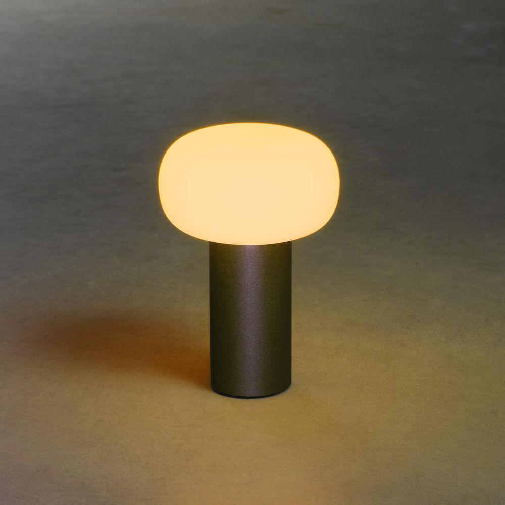 Eine moderne, pilzförmige Lampe auf dunkler Oberfläche, die ein warmes, gelbes Leuchten aussendet.