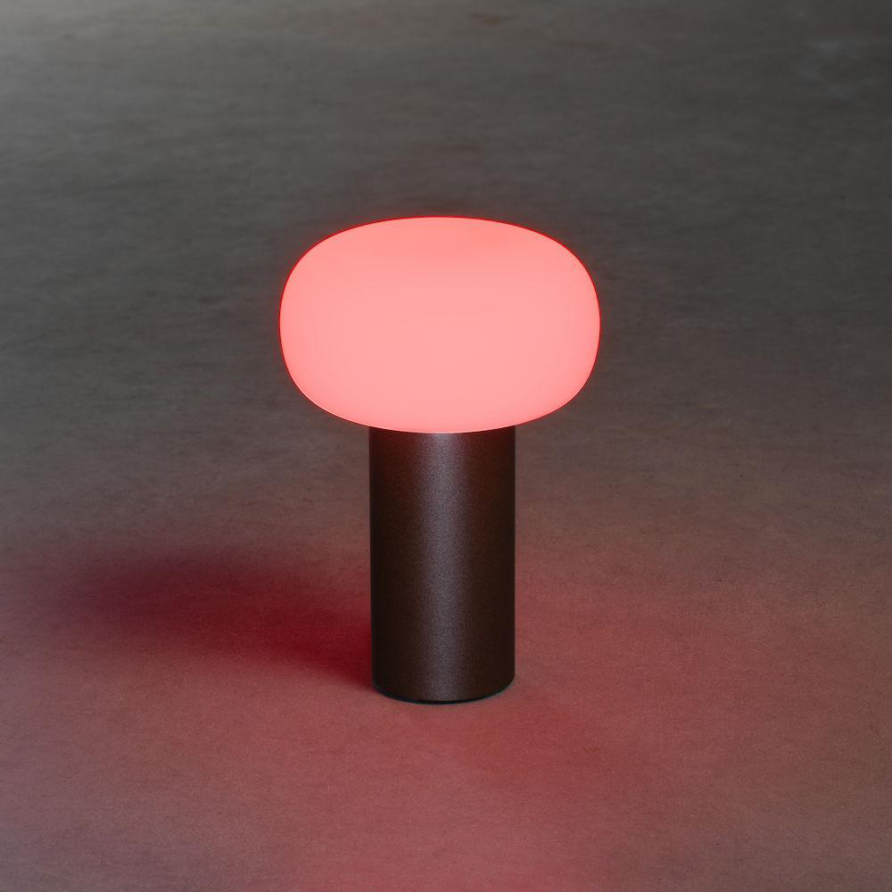 Eine rot leuchtende Tischlampe auf einem dunkelbraunen Sockel.