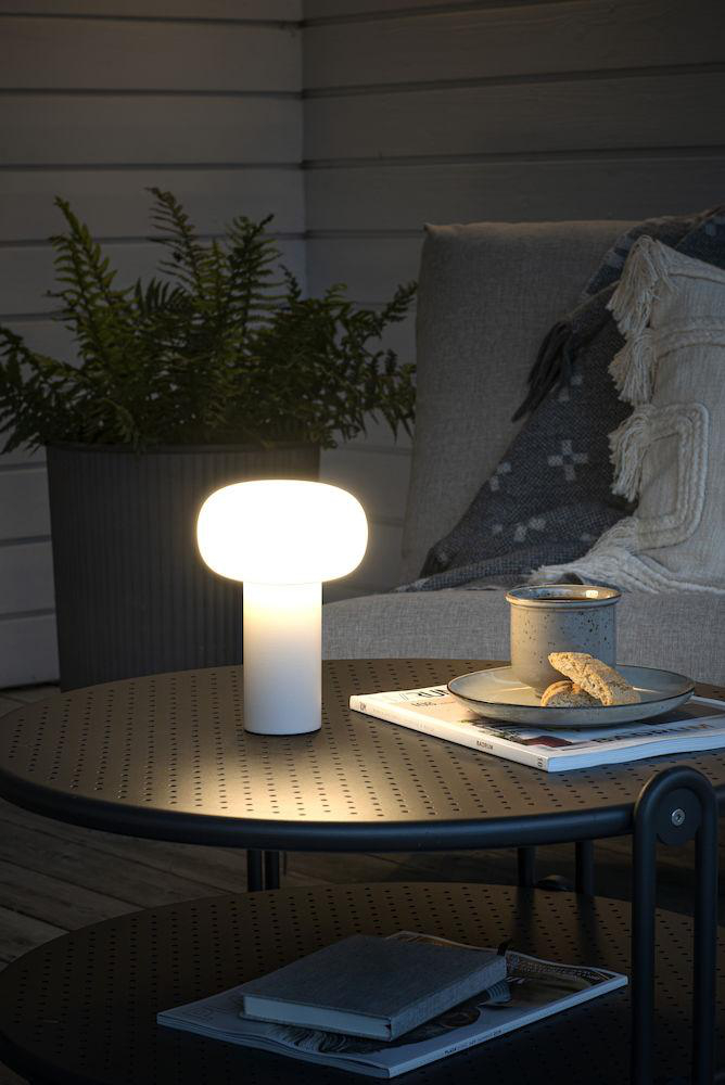 Weiße Tischlampe auf schwarzem Tisch mit Buch und Tasse. Outdoor-Szene.