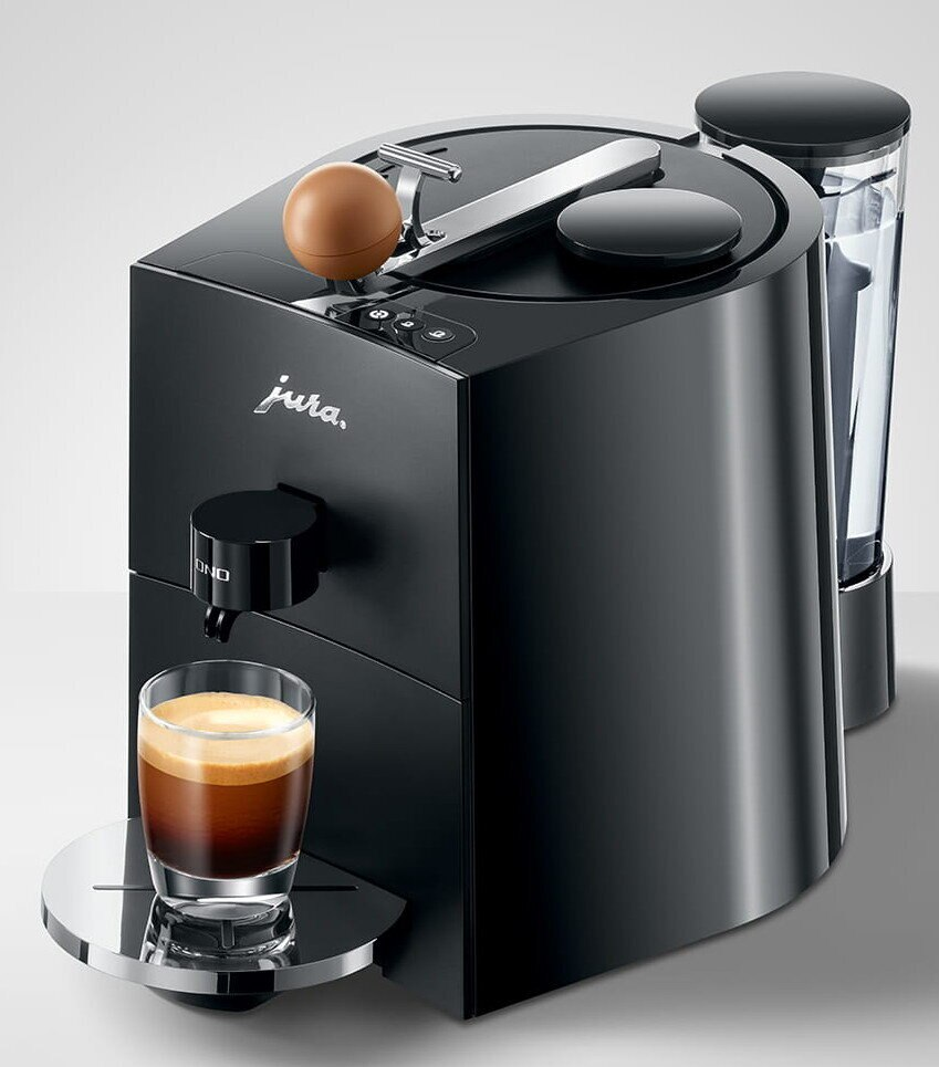 Czarny ekspres do kawy Jura ze szklanką espresso. Zbiornik na wodę po prawej.
