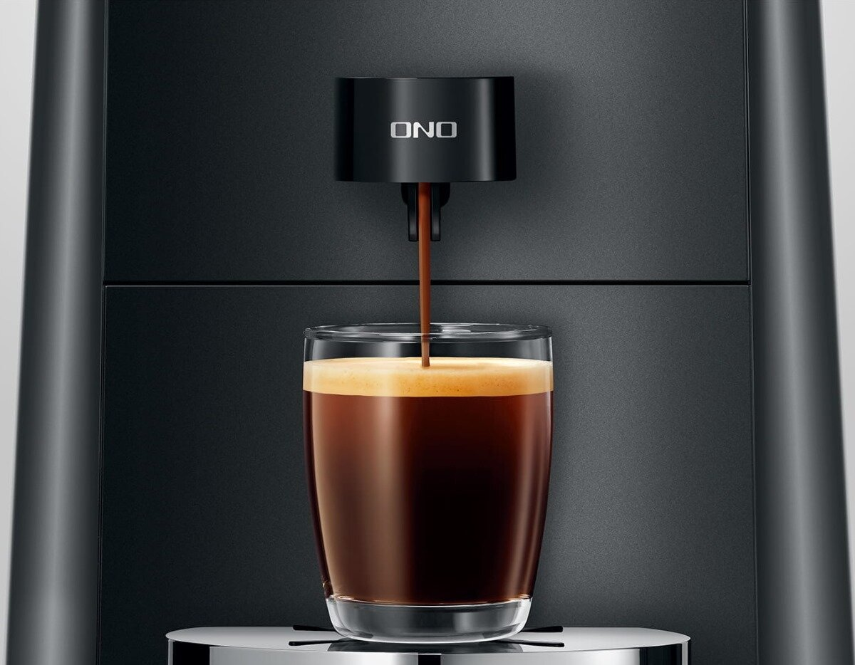 Czarny ekspres do kawy dozujący kawę do przezroczystej szklanki, z widoczną kawą.