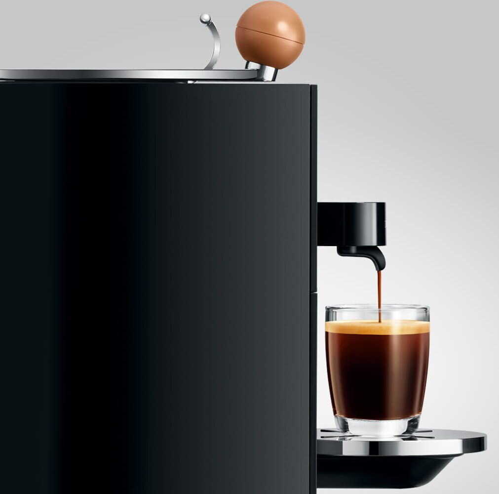 Ekspres do kawy wlewający kawę do szklanki. Ekspres jest czarny, kawa jest ciemna.