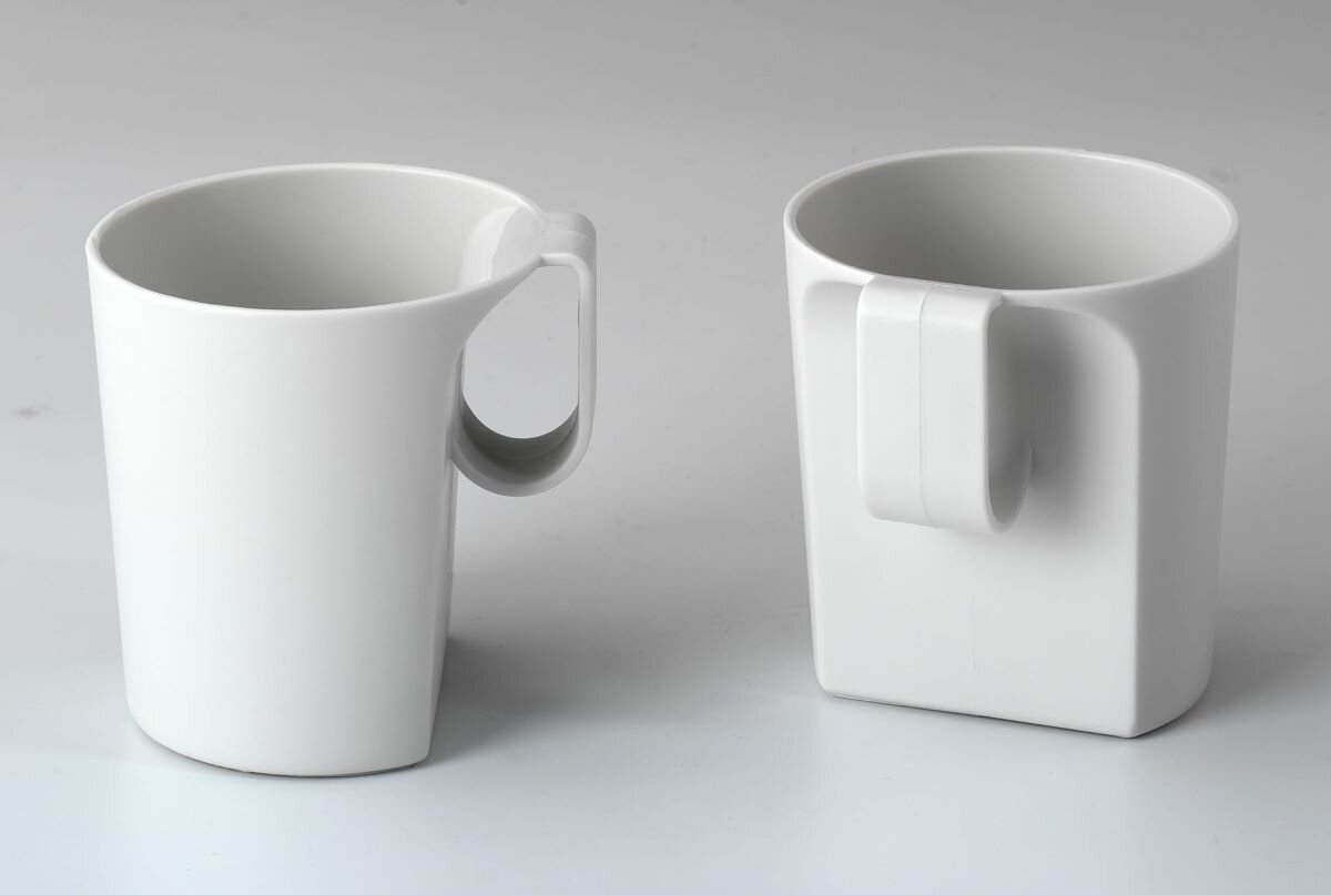 Dwa białe kubki z unikalnymi uchwytami. Jeden jest cylindryczny, drugi prostokątny. Oba stoją na białej powierzchni.