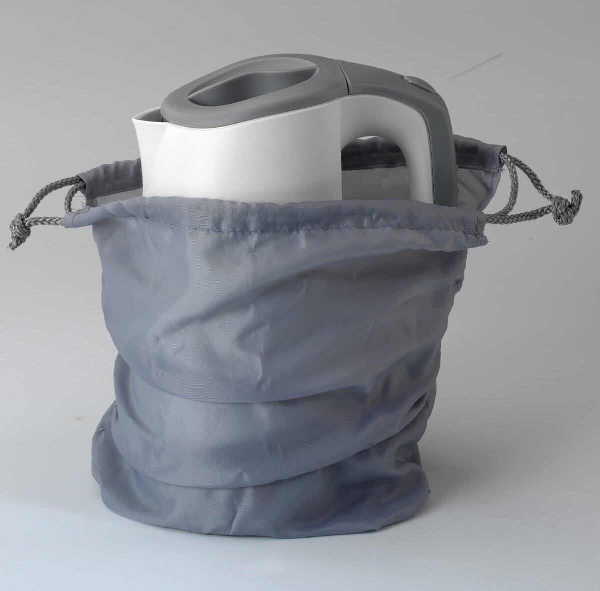Biały czajnik elektryczny z szarym uchwytem w szarej torbie ze sznurkiem, na tle szarego tła.
