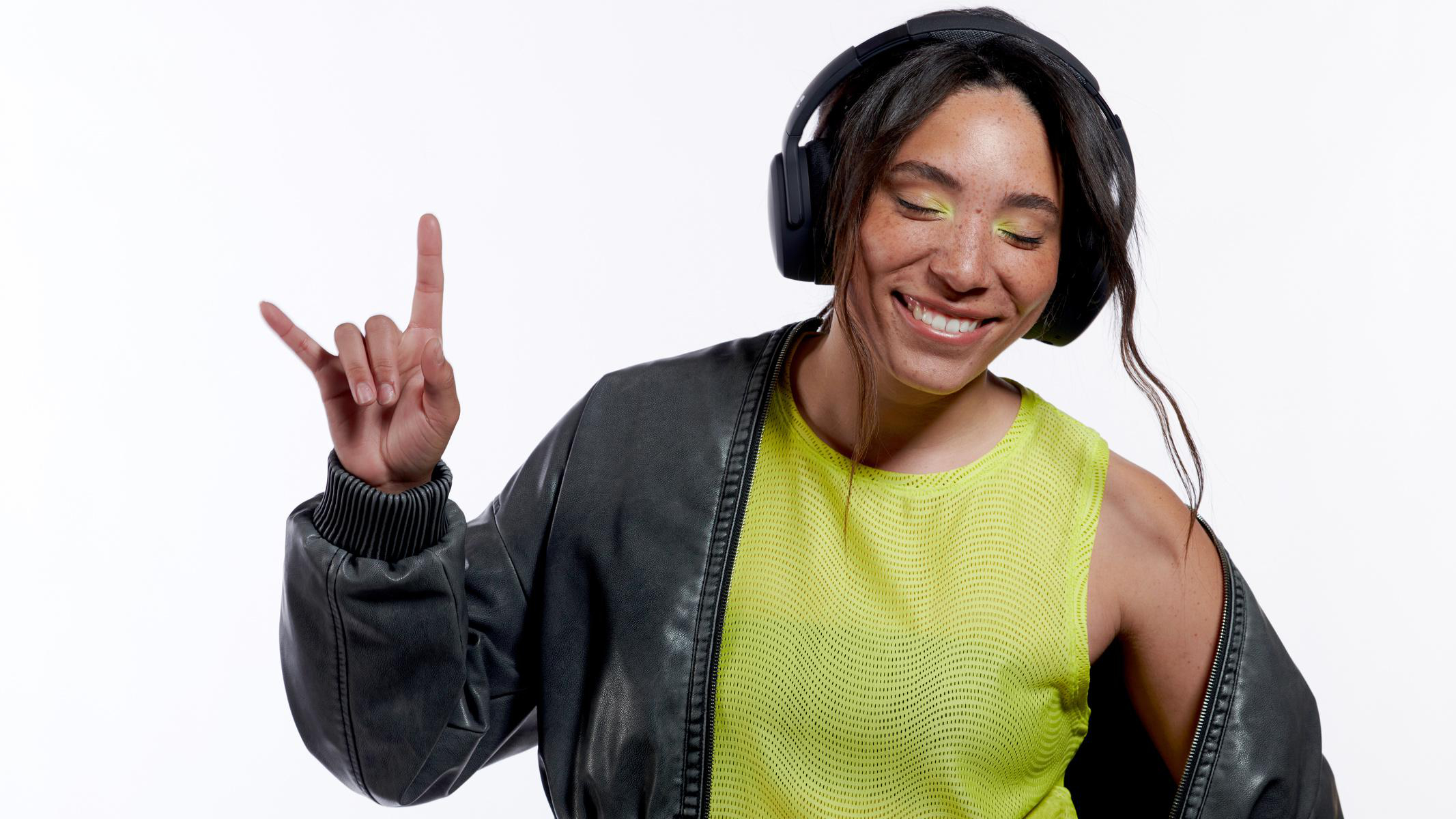 Eine Frau mit Kopfhörern lächelt und macht das Rock'n'Roll-Handzeichen, trägt eine Lederjacke.