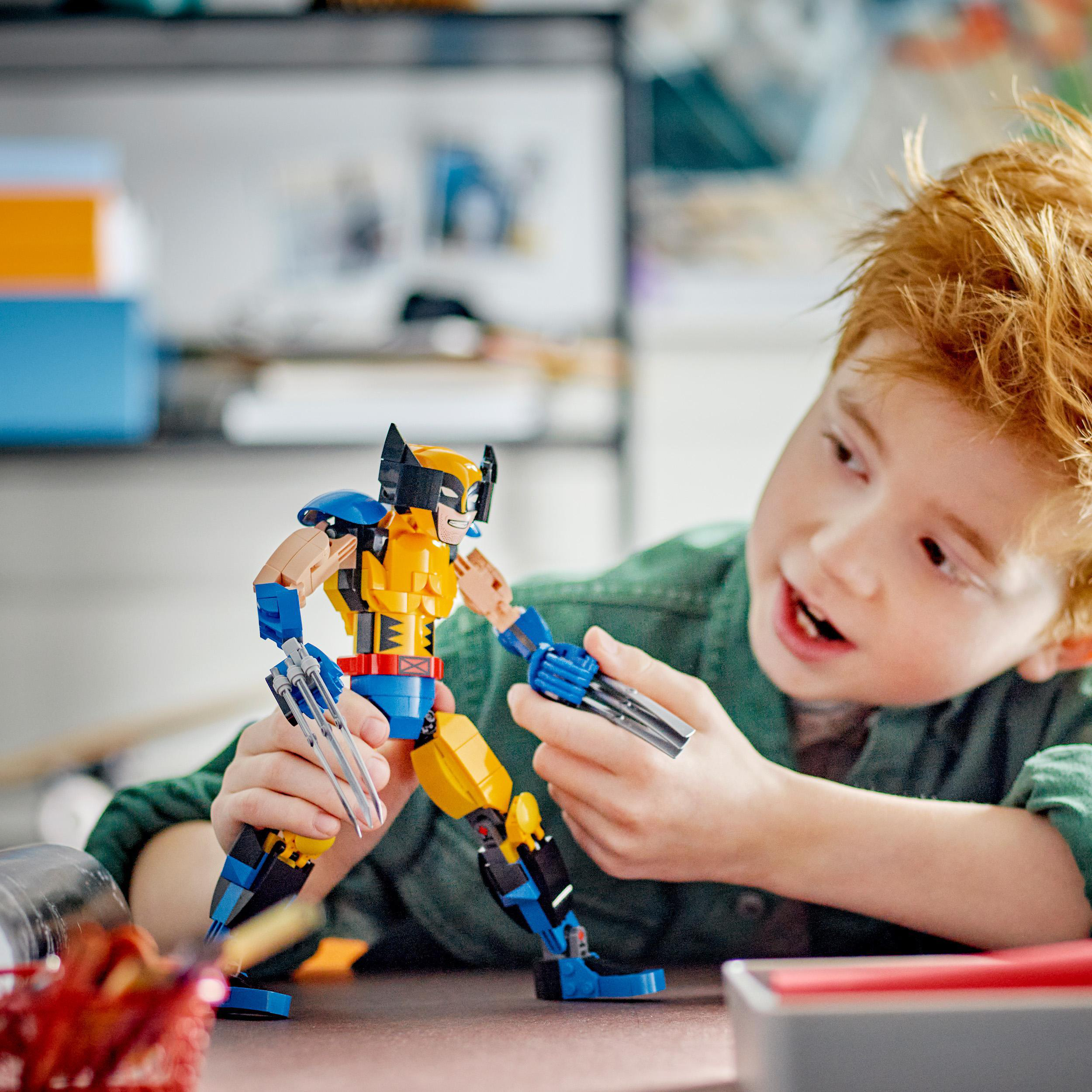 Ein Junge spielt mit einer Lego Wolverine Figur, hält die Krallen und sieht aufgeregt aus.